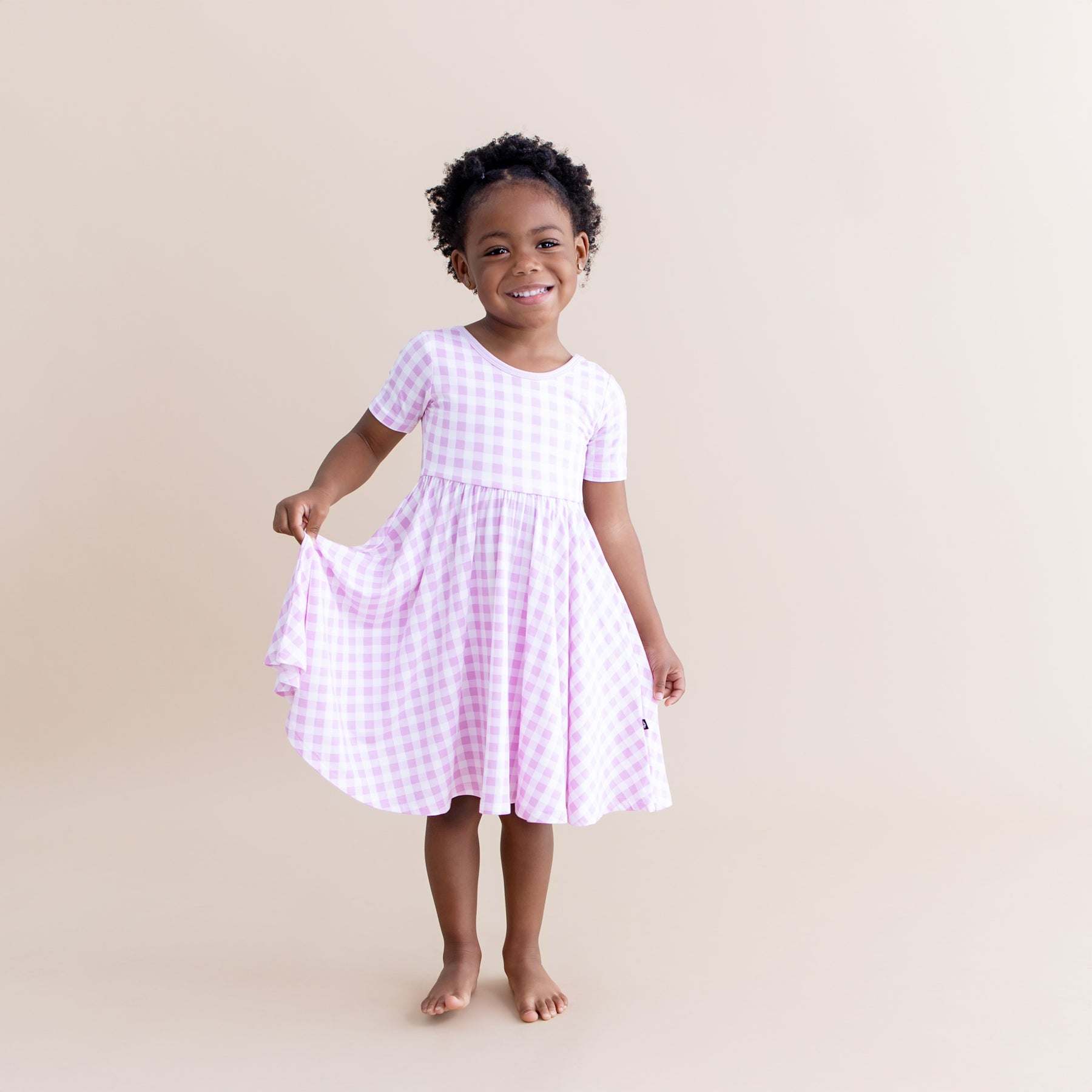 Young smiling girl wearing the Twirl Dress in Gingham Thistle holding out the skirt of the dress
