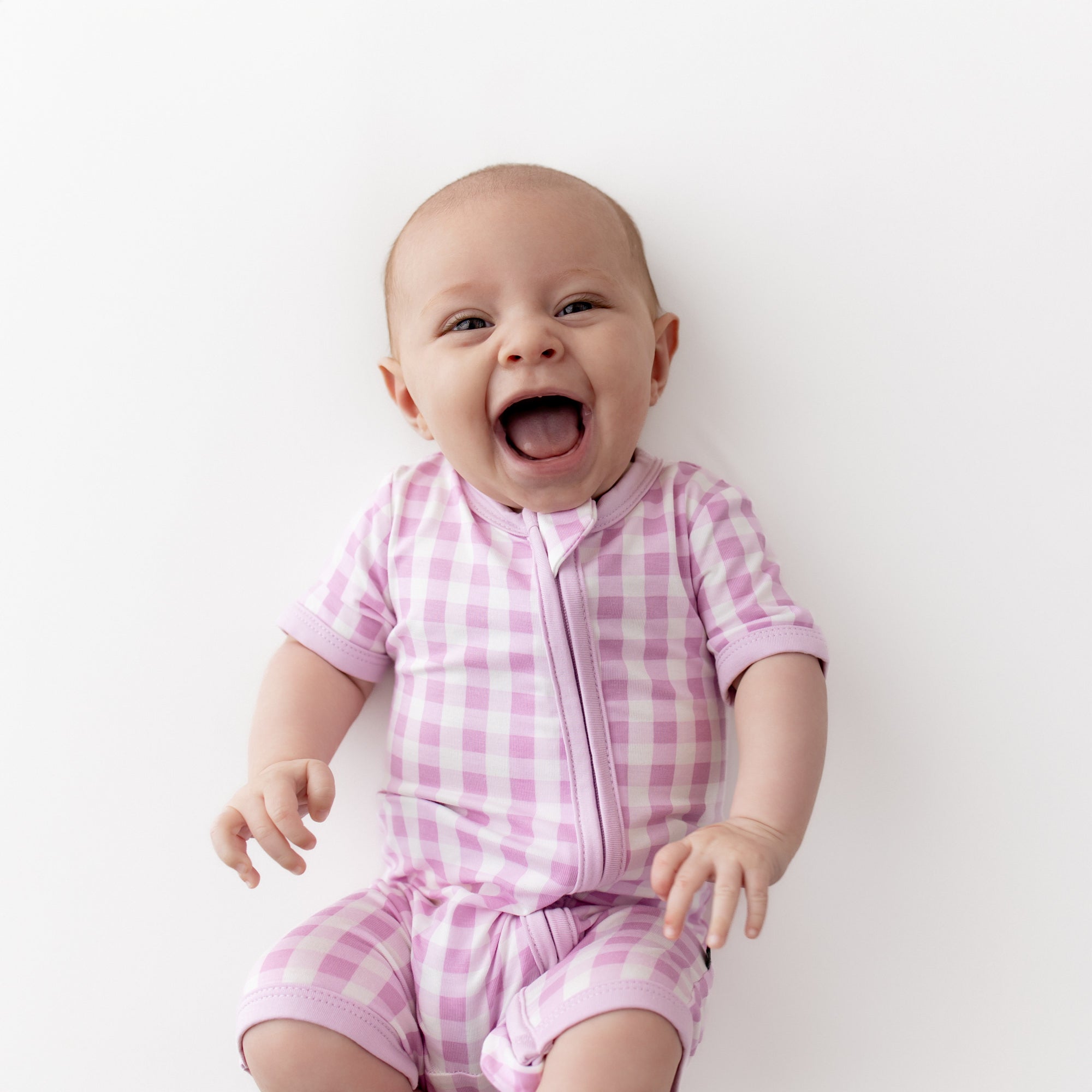 Smiling infant wearing the Zipper Shortall Romper in Gingham Thistle