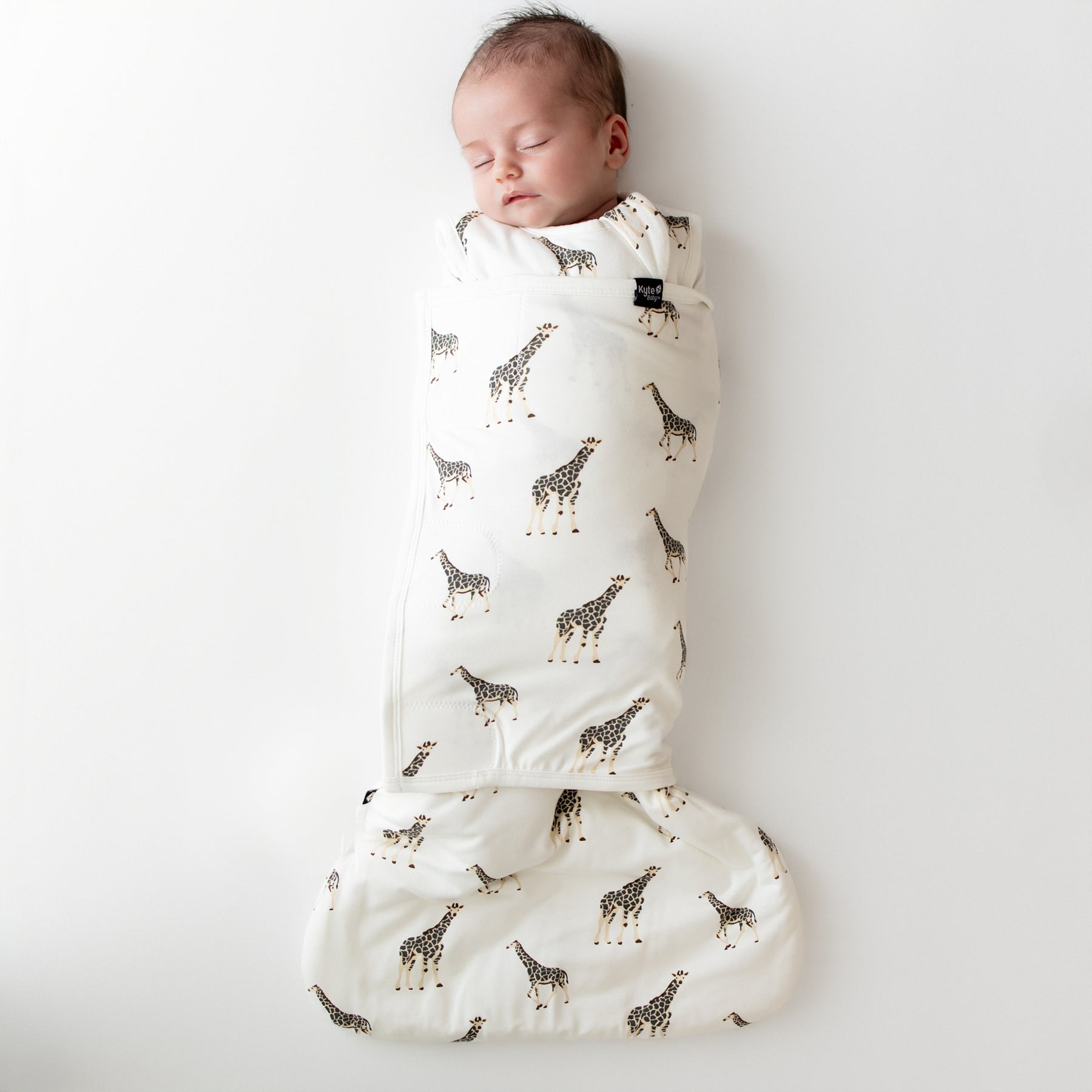 Newborn baby swaddled in a white swaddler with giraffe pattern on a plain background