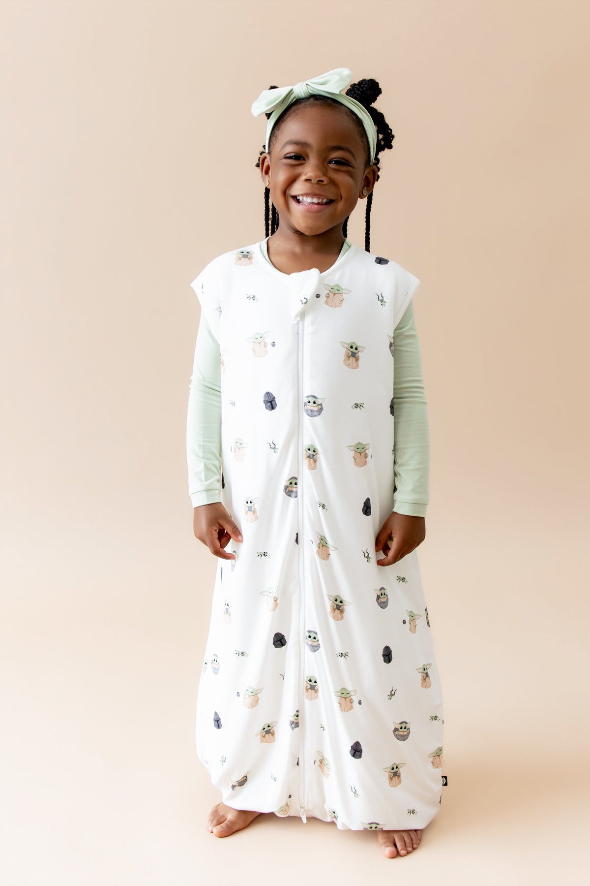 Smiling girl wearing the Sleep Bag Walker in Grogu™ 1.0 with light green long sleeve pajamas on underneath