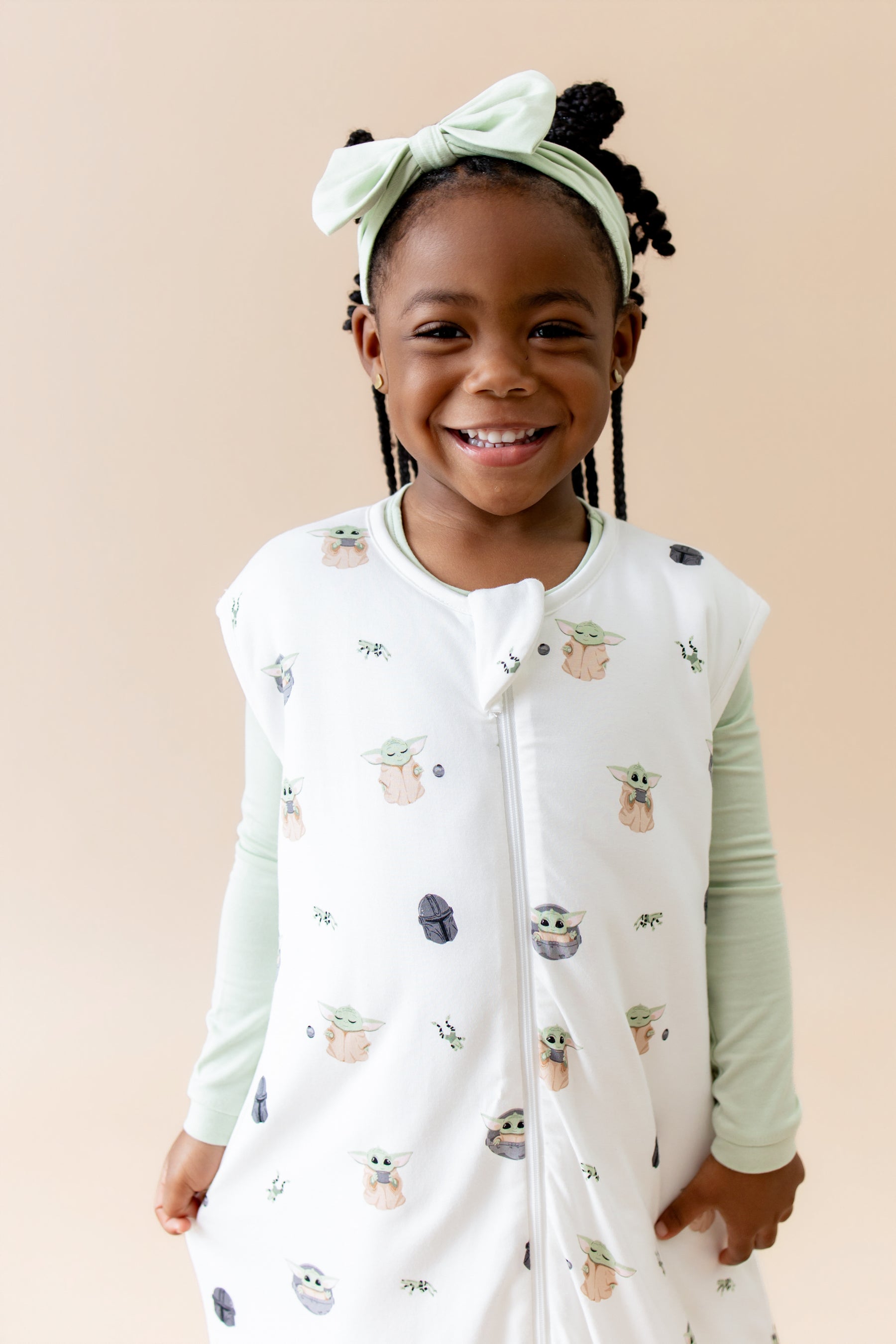 Close up of smiling girl wearing the Sleep Bag Walker in Grogu™ 1.0 with light green long sleeve pajamas on underneath