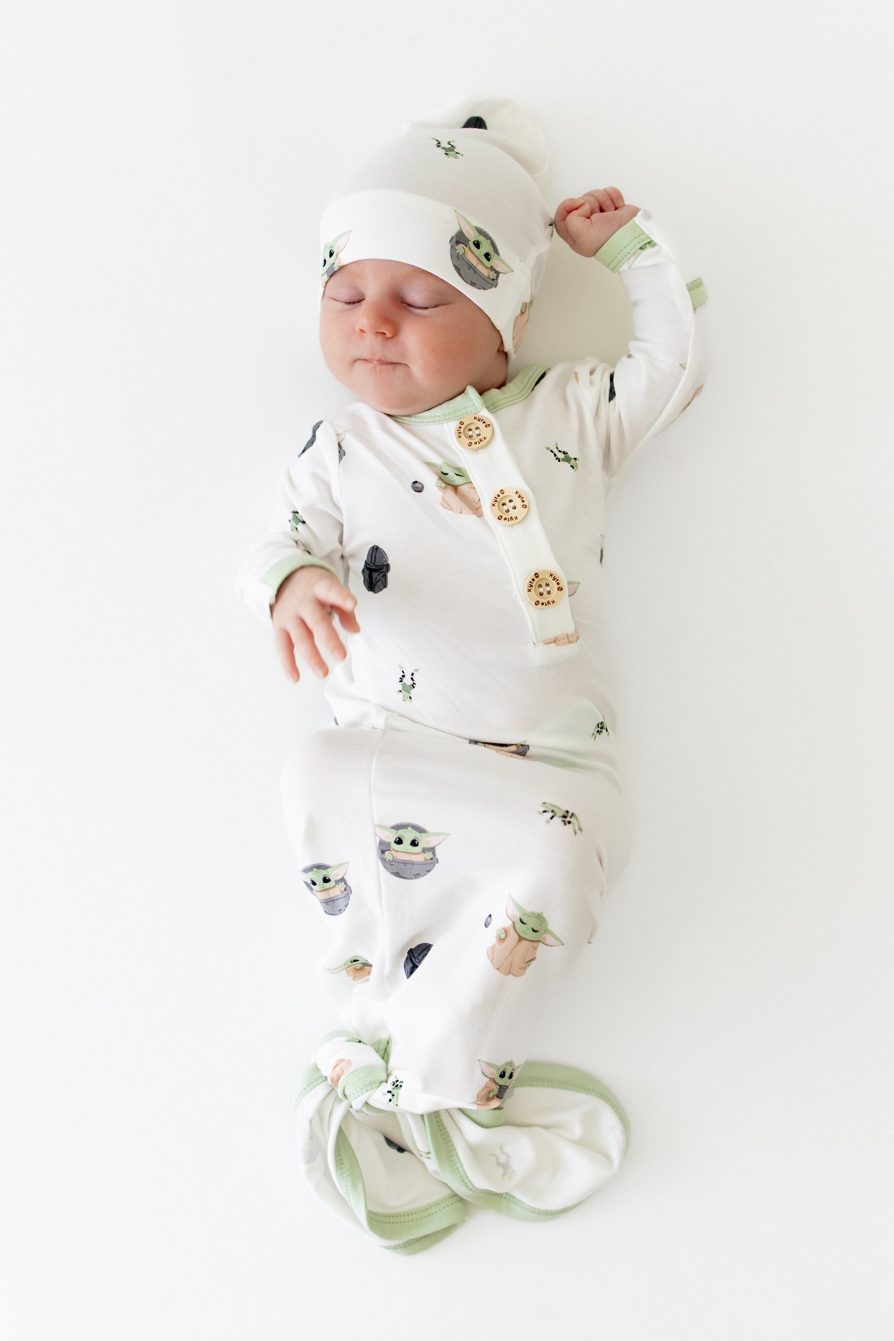 Sleeping newborn with one arm up at their head wearing the Knotted Gown with Hat Set in Grogu™
