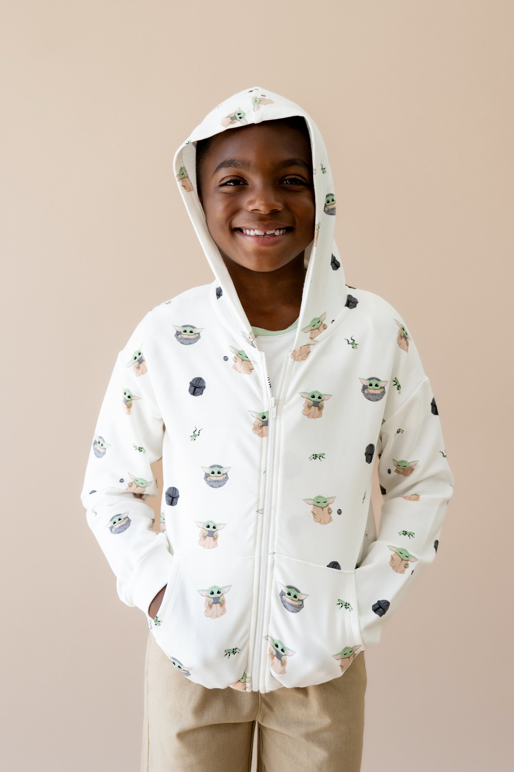 Young boy wearing the Zip-Up Hoodie in Grogu™ with the hood up and his hands in the pockets