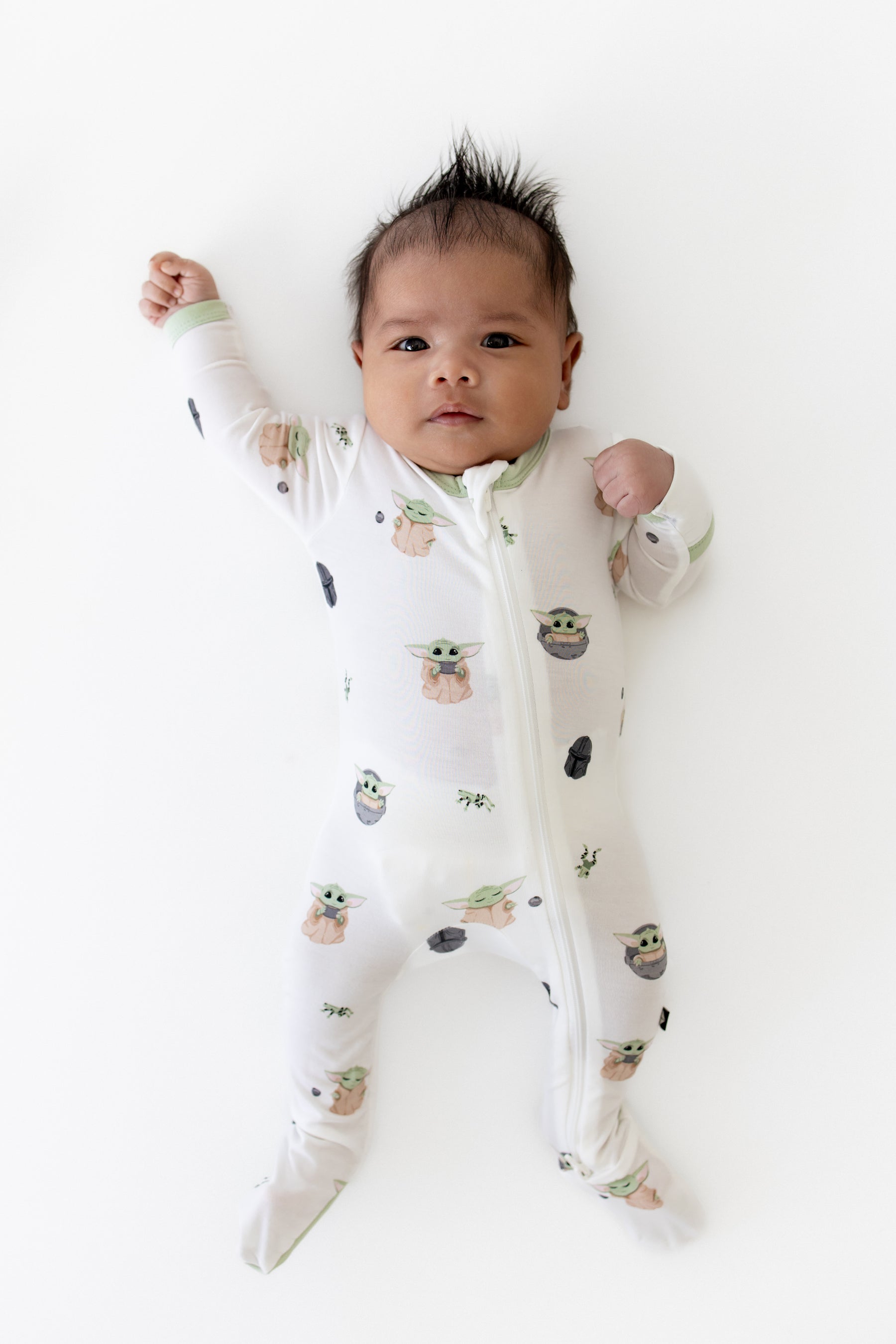 Infant laying on a white surface wearing the Zippered Footie in Grogu™
