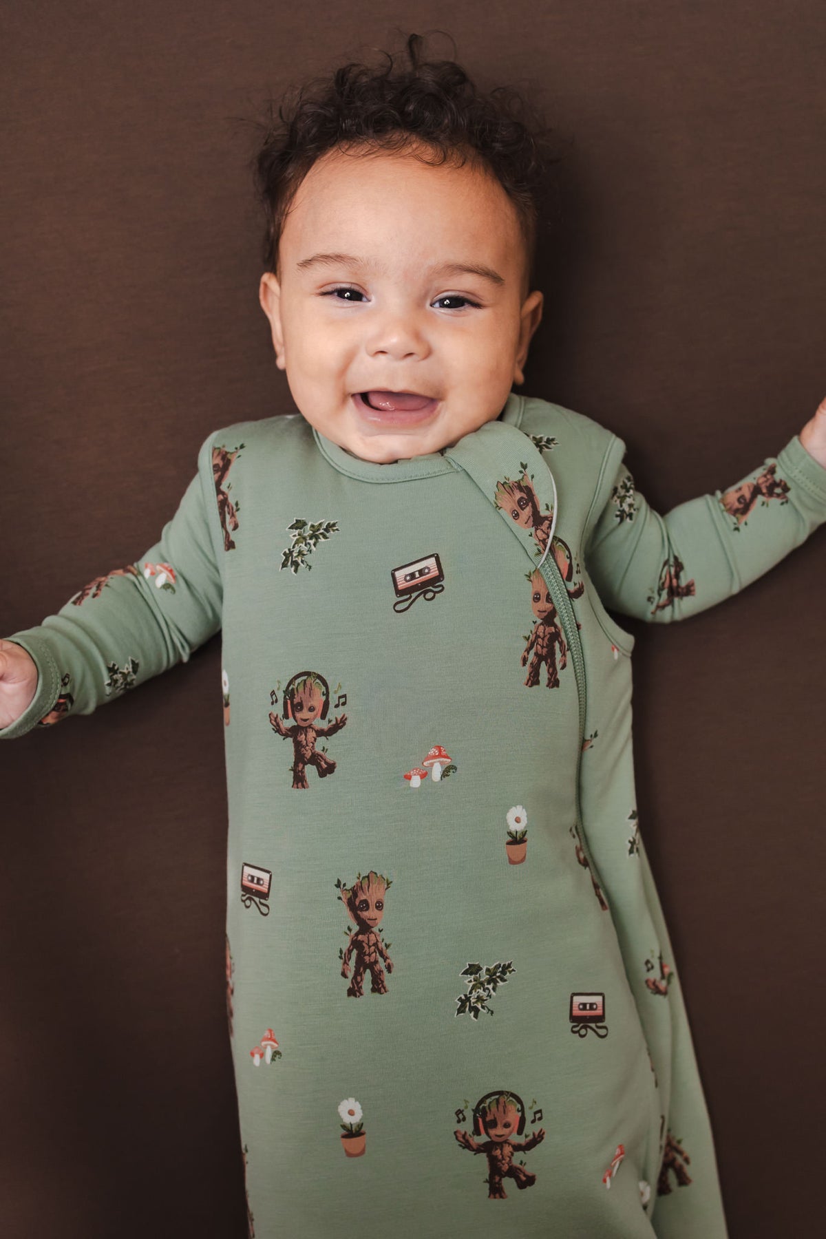 Baby smiling in Green Sleep Bag in Groot 1.0 lying on a brown background