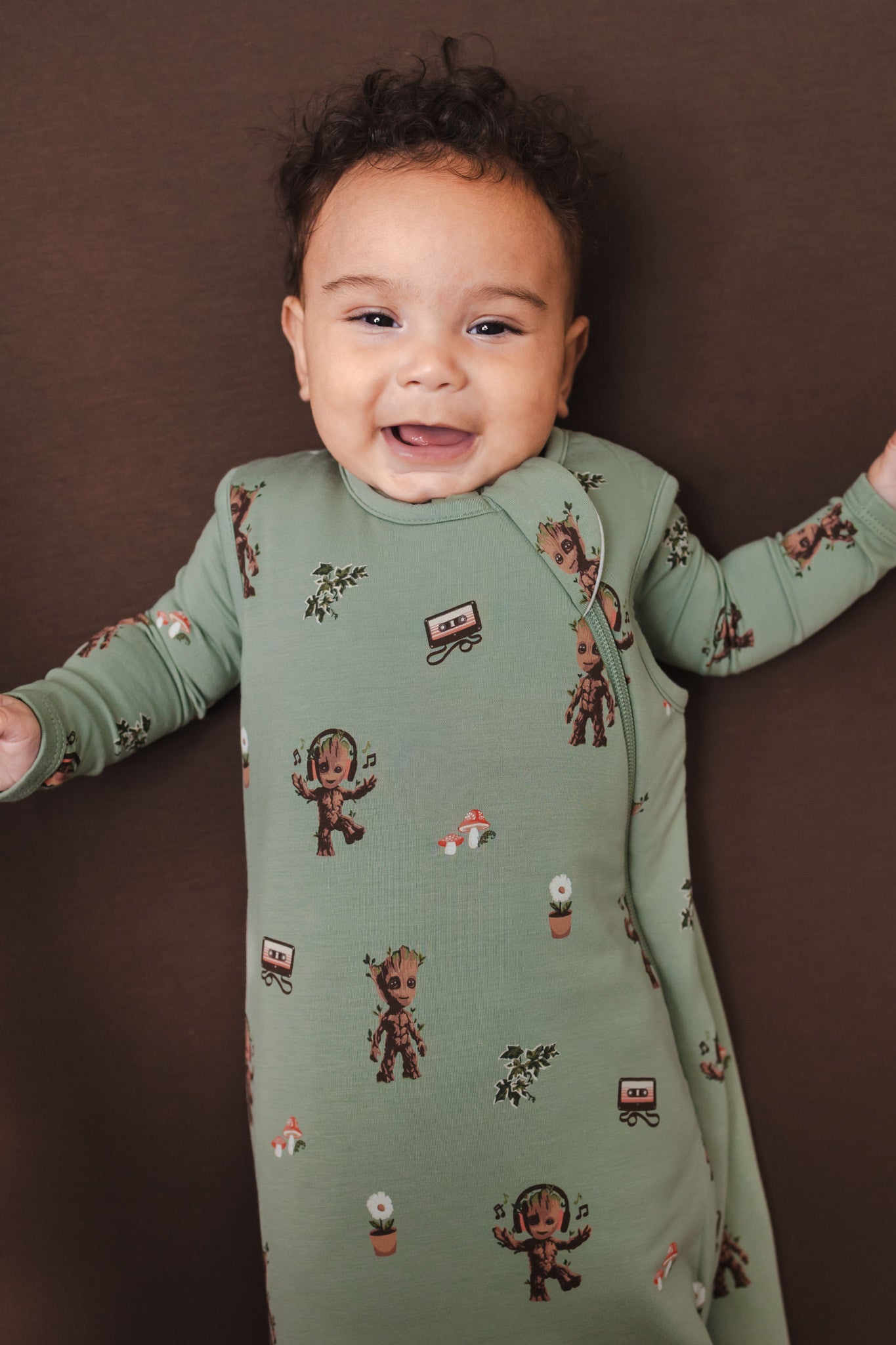 Baby smiling in Green Sleep Bag in Groot 1.0 lying on a brown background