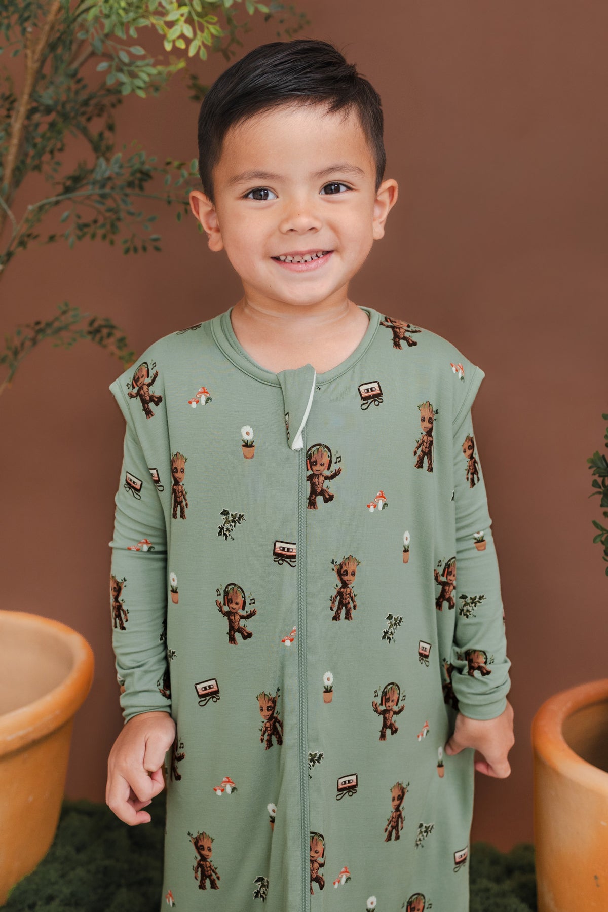 Boy wearing Green Sleep Bag Walker in Groot 1.0 print standing between green plant pots