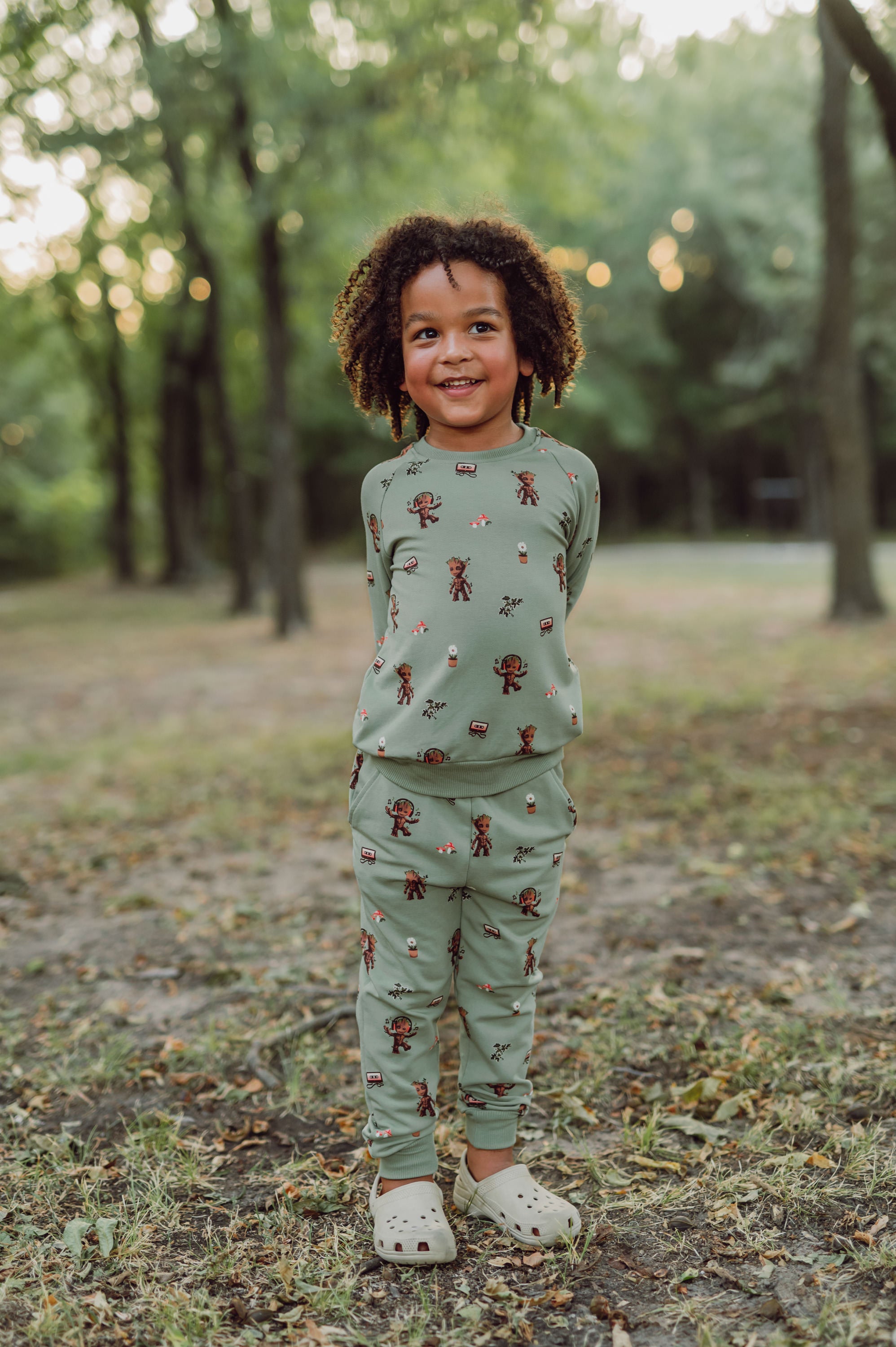 boy outside with his hands behind his back wearing groot jogger set and smiling.