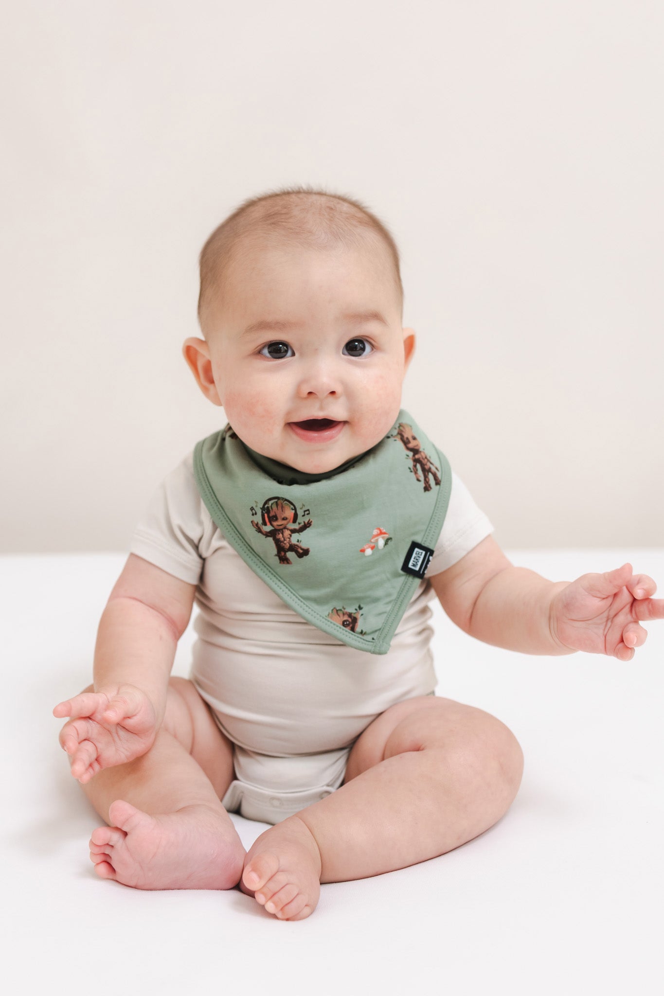 Baby wearing Green Bib in Groot print over a beige bodysuit sitting on a beige background