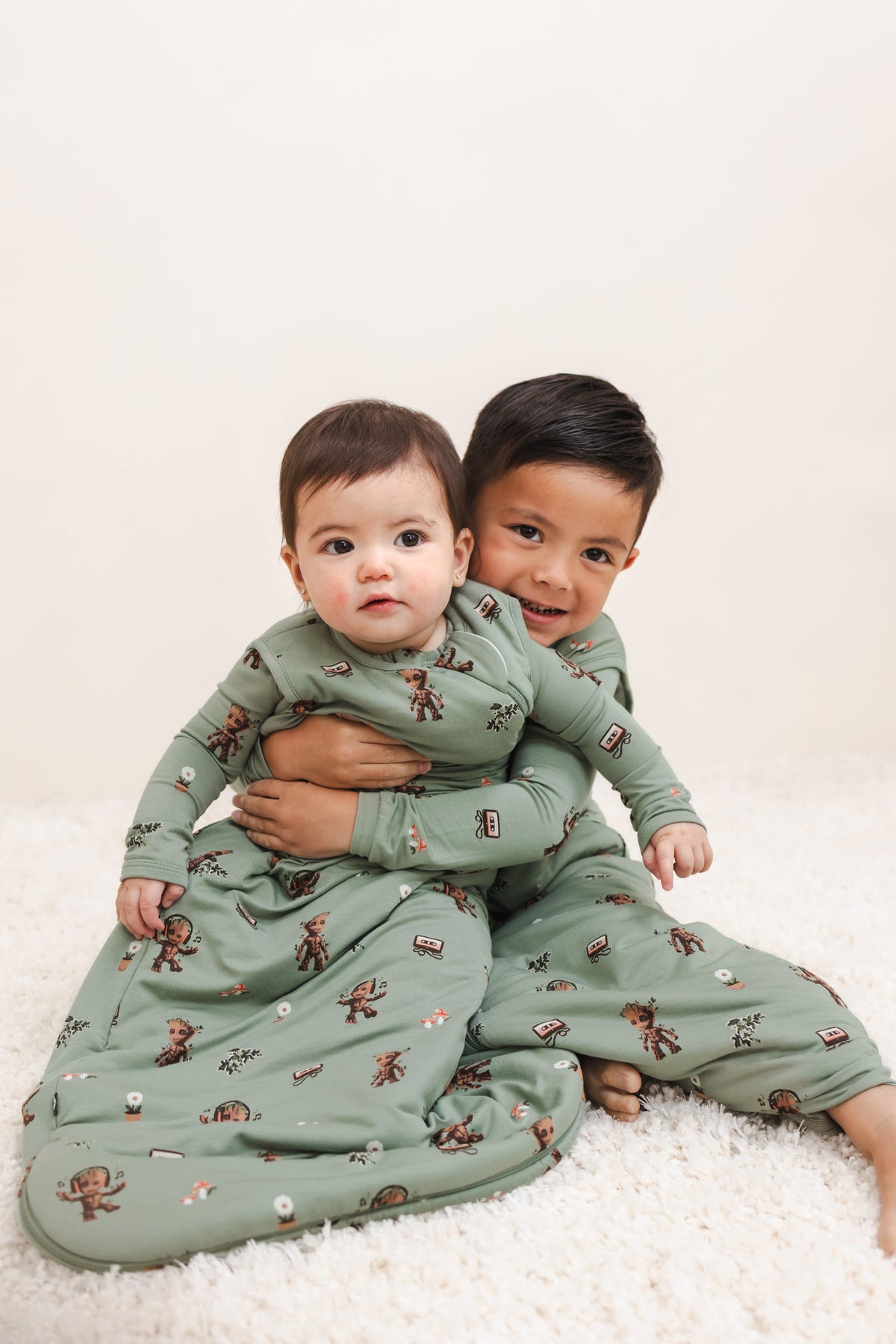 A Baby and a boy cuddled together wearing Green Sleep bag and Sleep Bag Walker in Groot 1.0 print on a beige background
