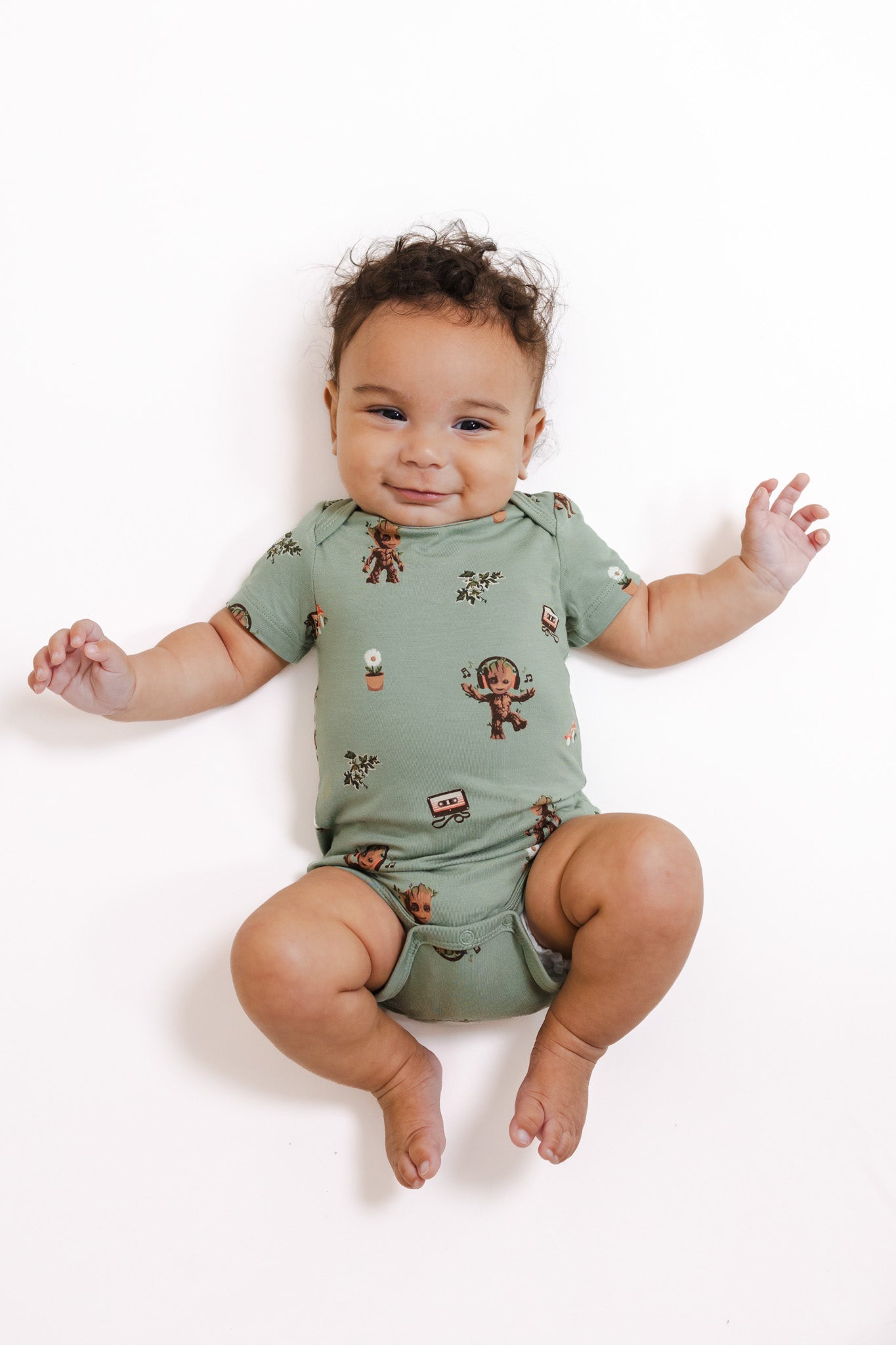 Baby wearing Green Bodysuit in Groot print lying on a white background