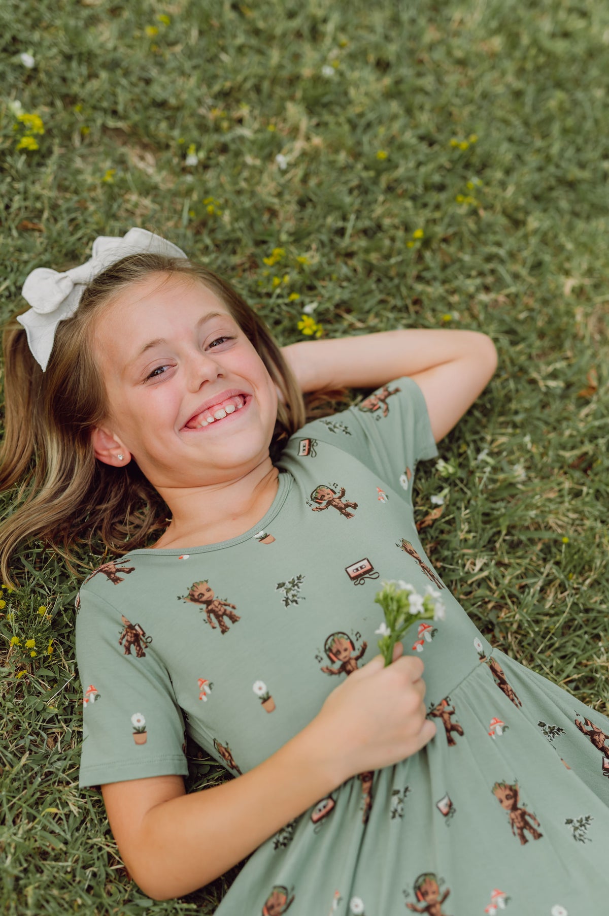 Girl lying on grass wearing Twirl Dress in Groot print