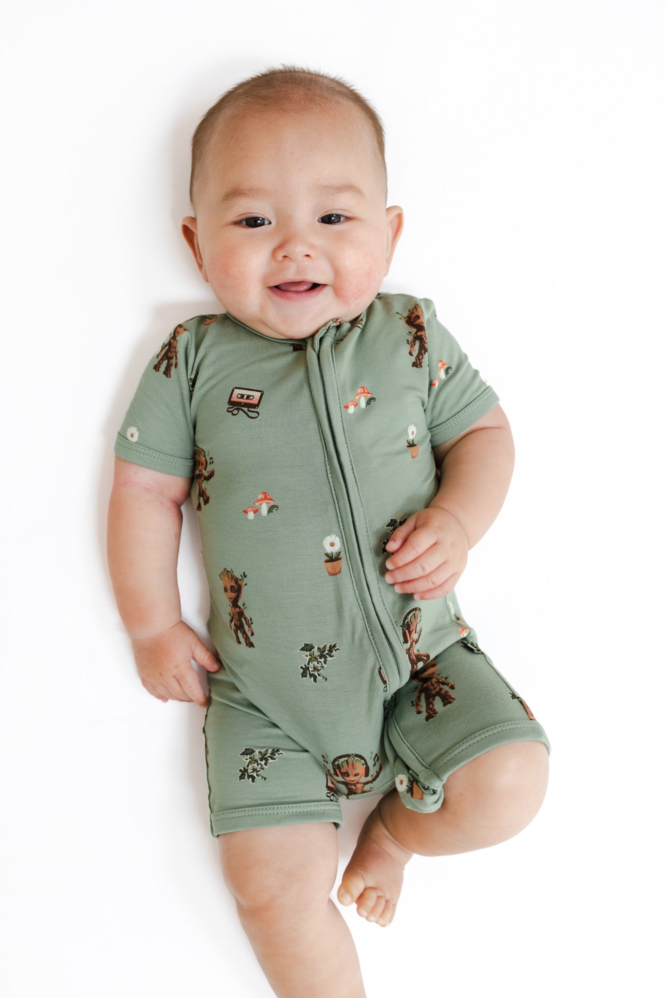 Baby in Green Zipper Shortall Romper in Groot print lying on a white background