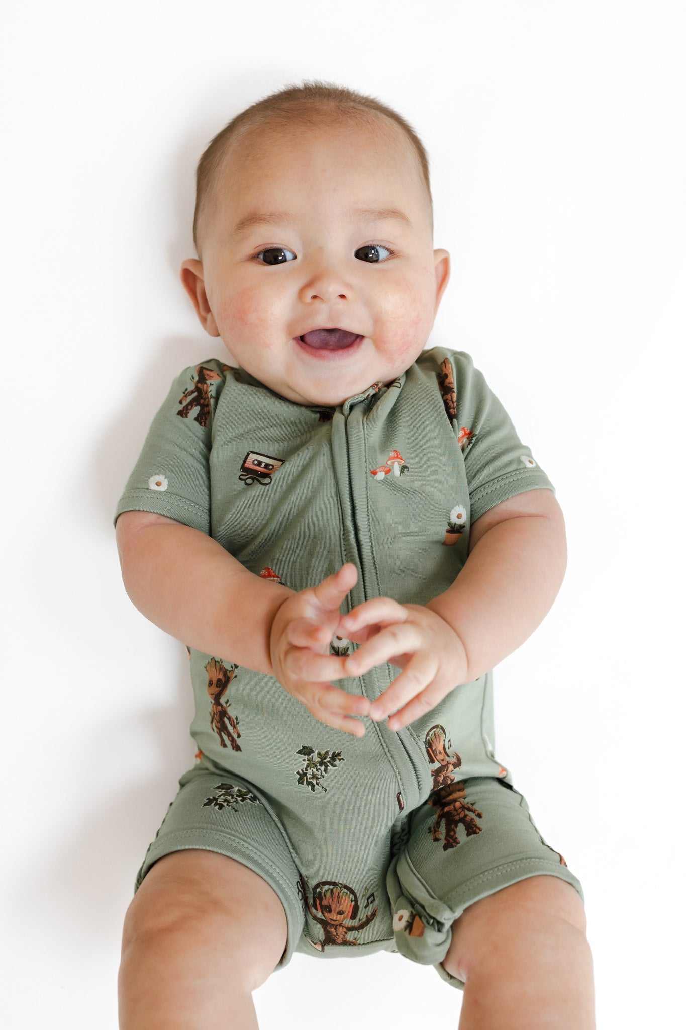 Baby wearing Green Zipper Shortall Romper in Groot print lying on a white background