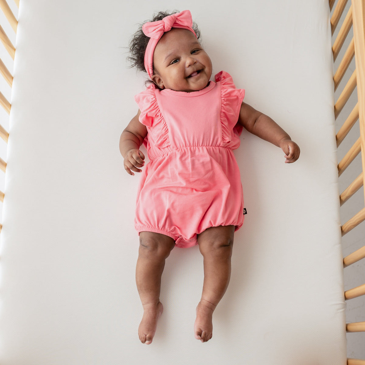 baby smiling while wearing kyte baby bubble romper and bow in guava 