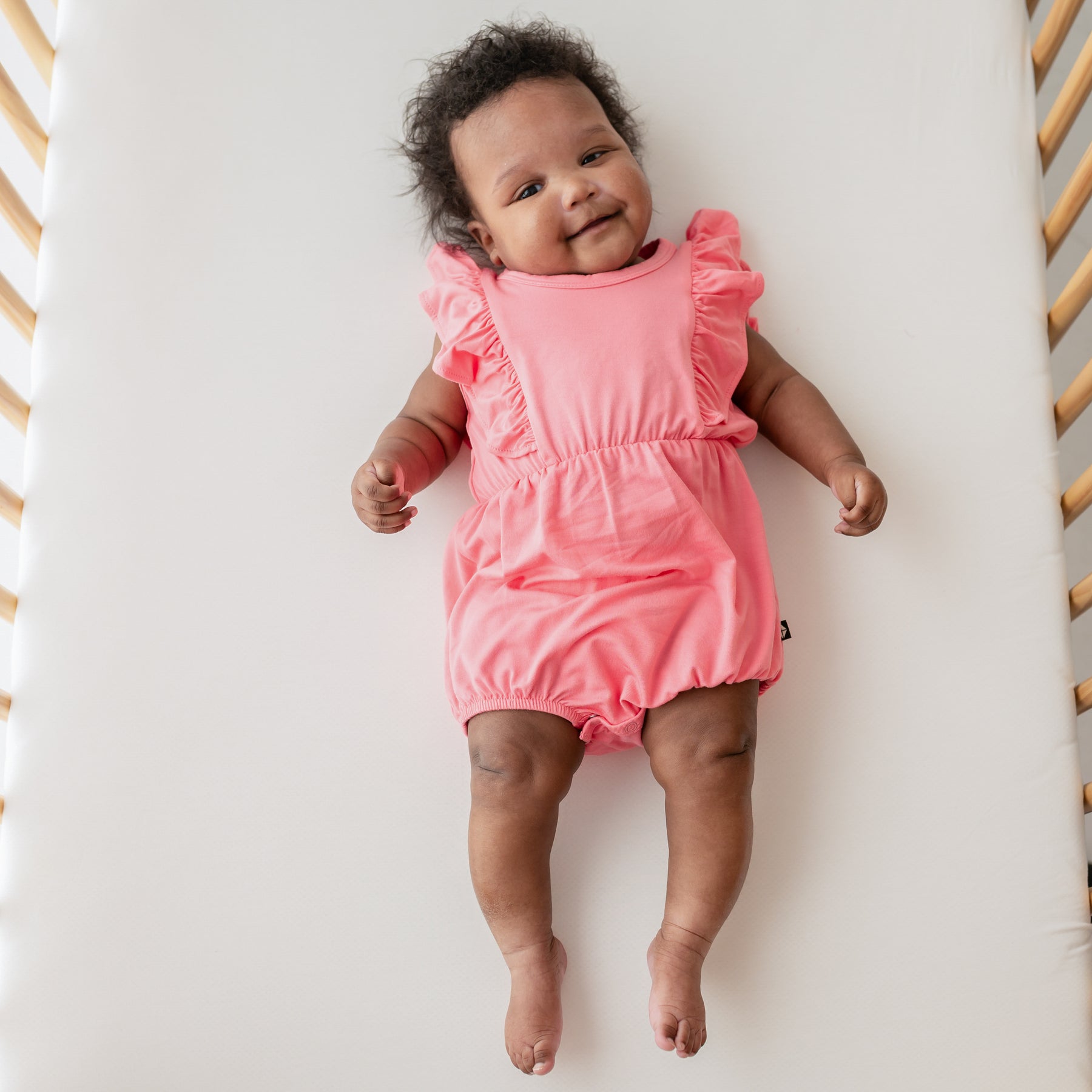 baby in crib wearing guava bubble romper