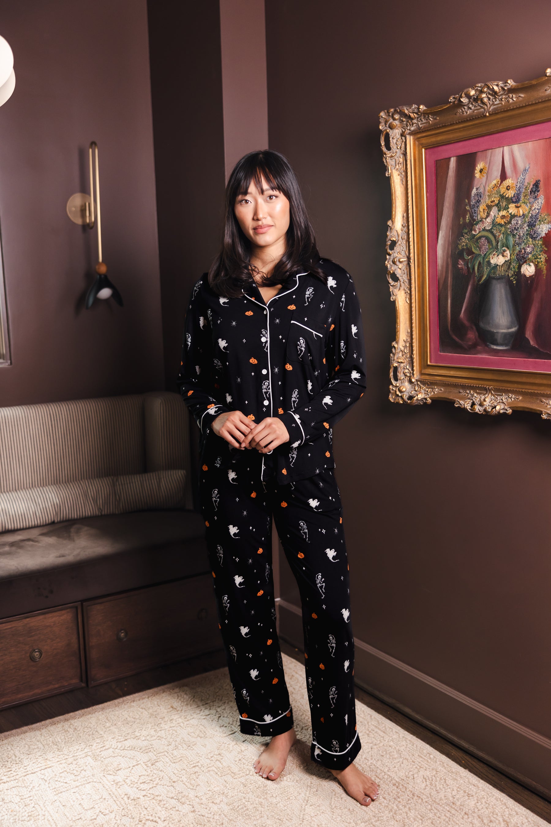 Modal wearing Black Long-Sleeved Women's Pajama Set in Halloween Friends print standing in a living room 