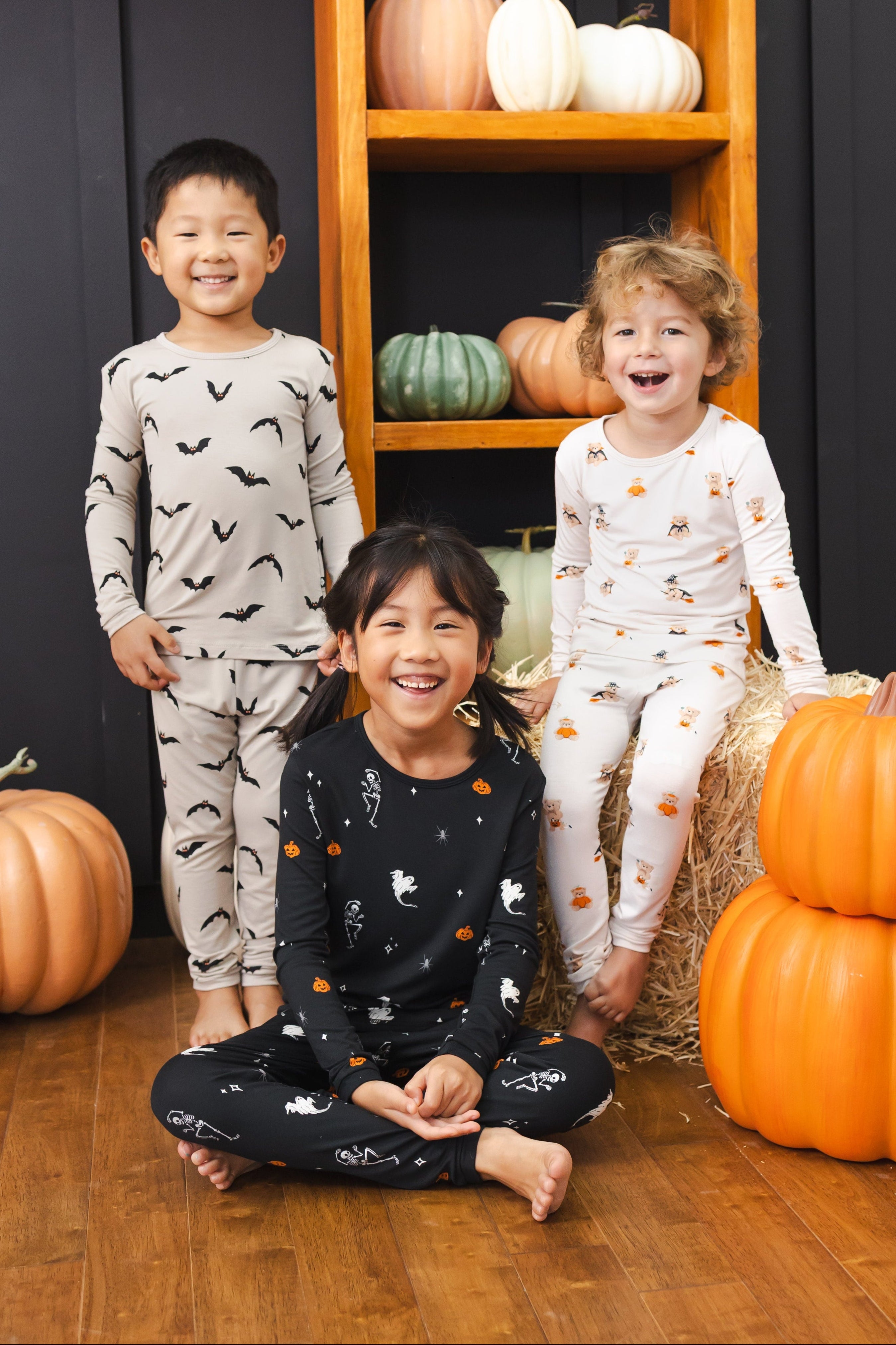 Three toddlers standing together in Halloween pumpkin decorations wearing long sleeve pajama set in Bats, Halloween Teddy and Halloween Friends prints