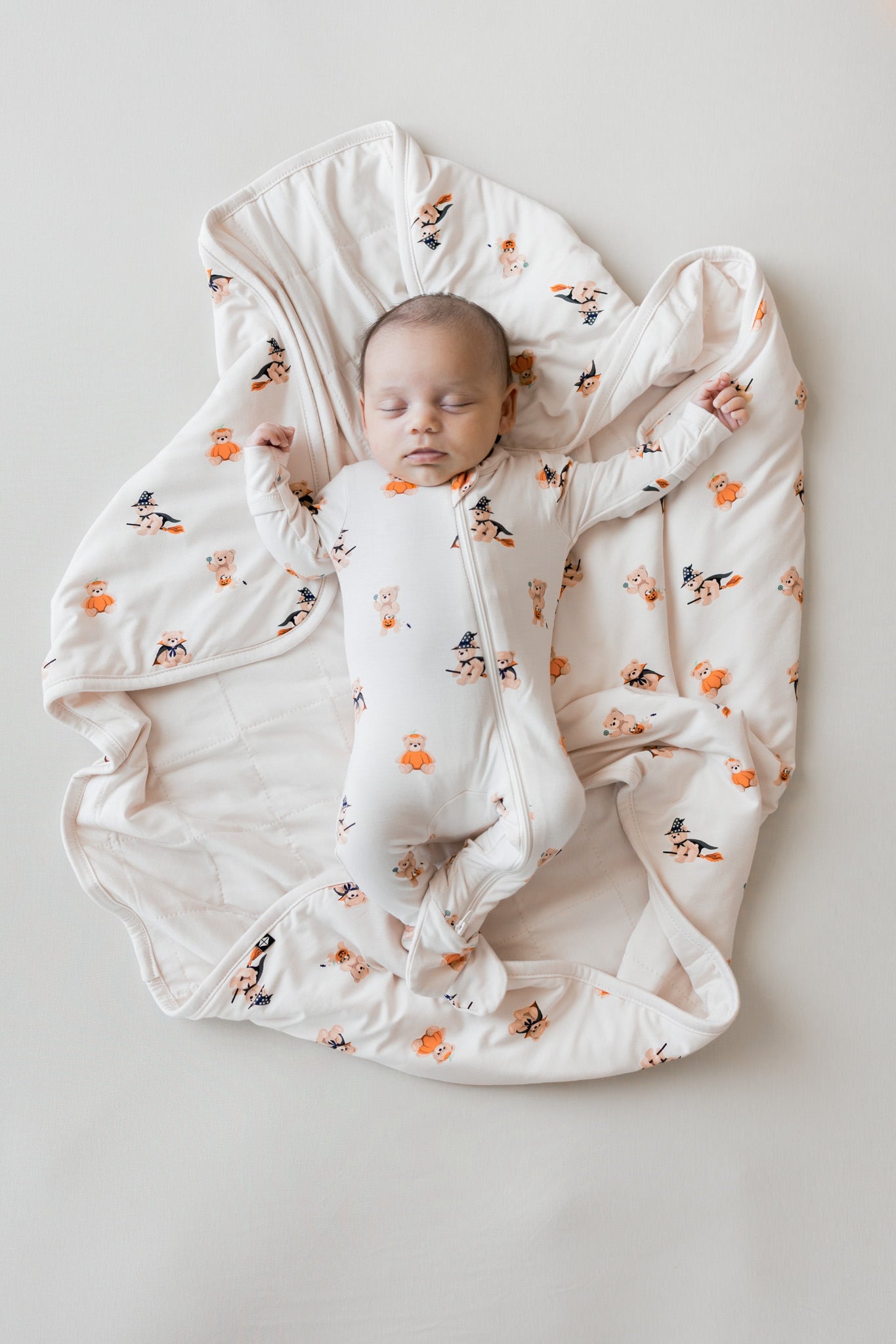 Baby sleeping on Baby Blanket in Halloween Teddy 1.0 print wearing a similar print zippered footie on a beige background