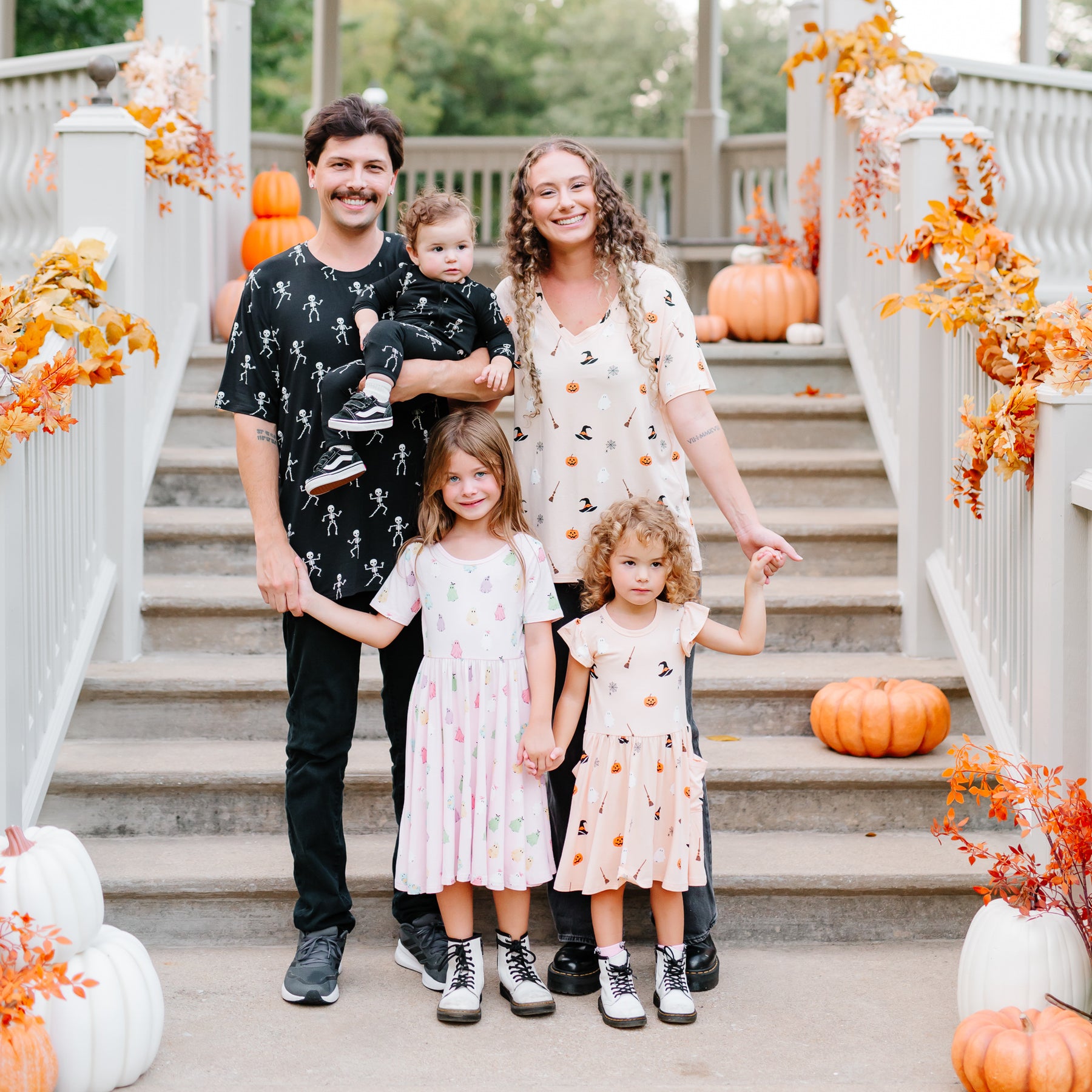 Family of five standing wearing halloween printed clothing on steps decorated with pumpkins and autumn leaves