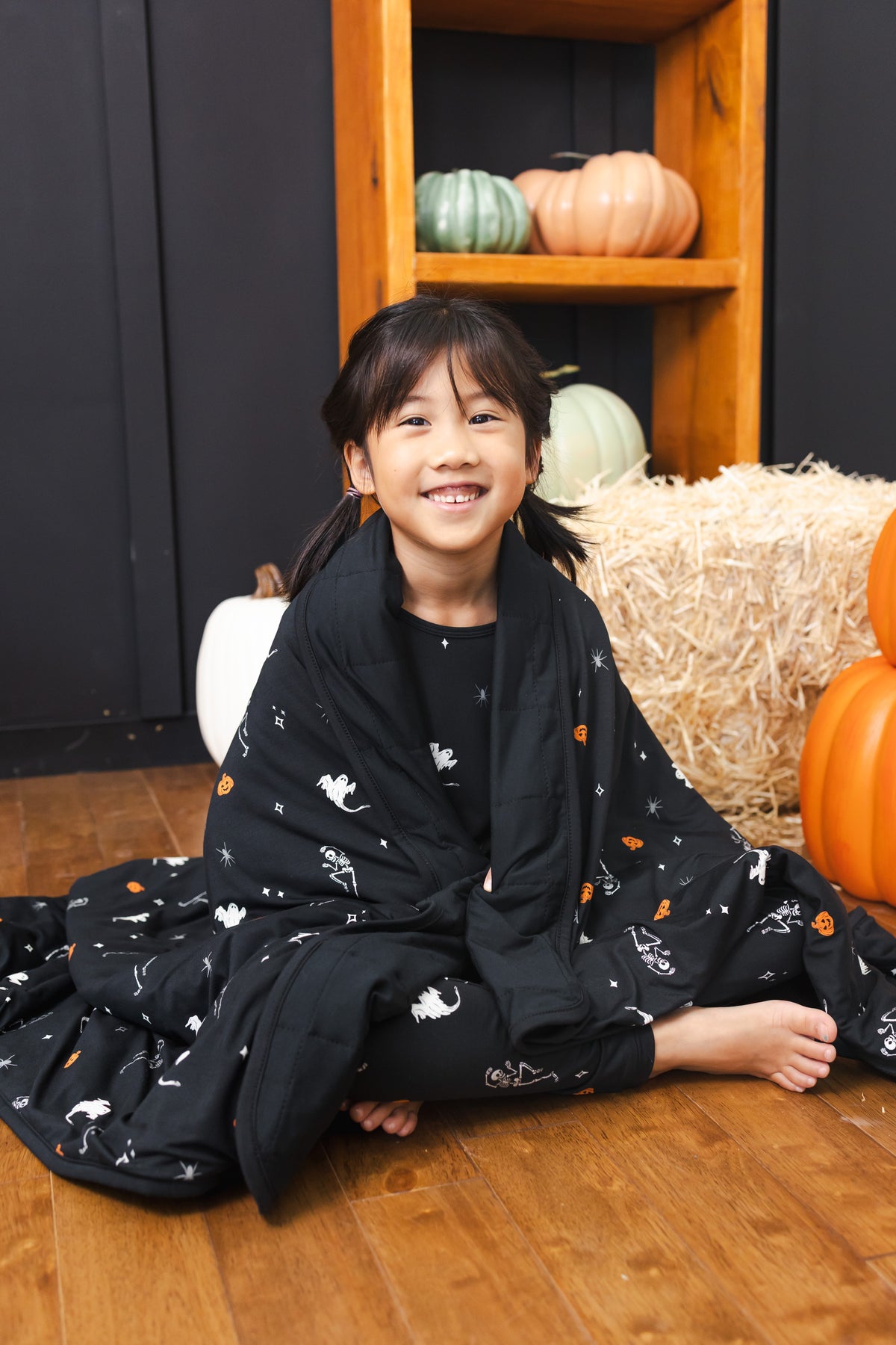 Girl wrapped in Toddler Blanket in Halloween Friends 1.0 print sitting in front of Halloween decorations