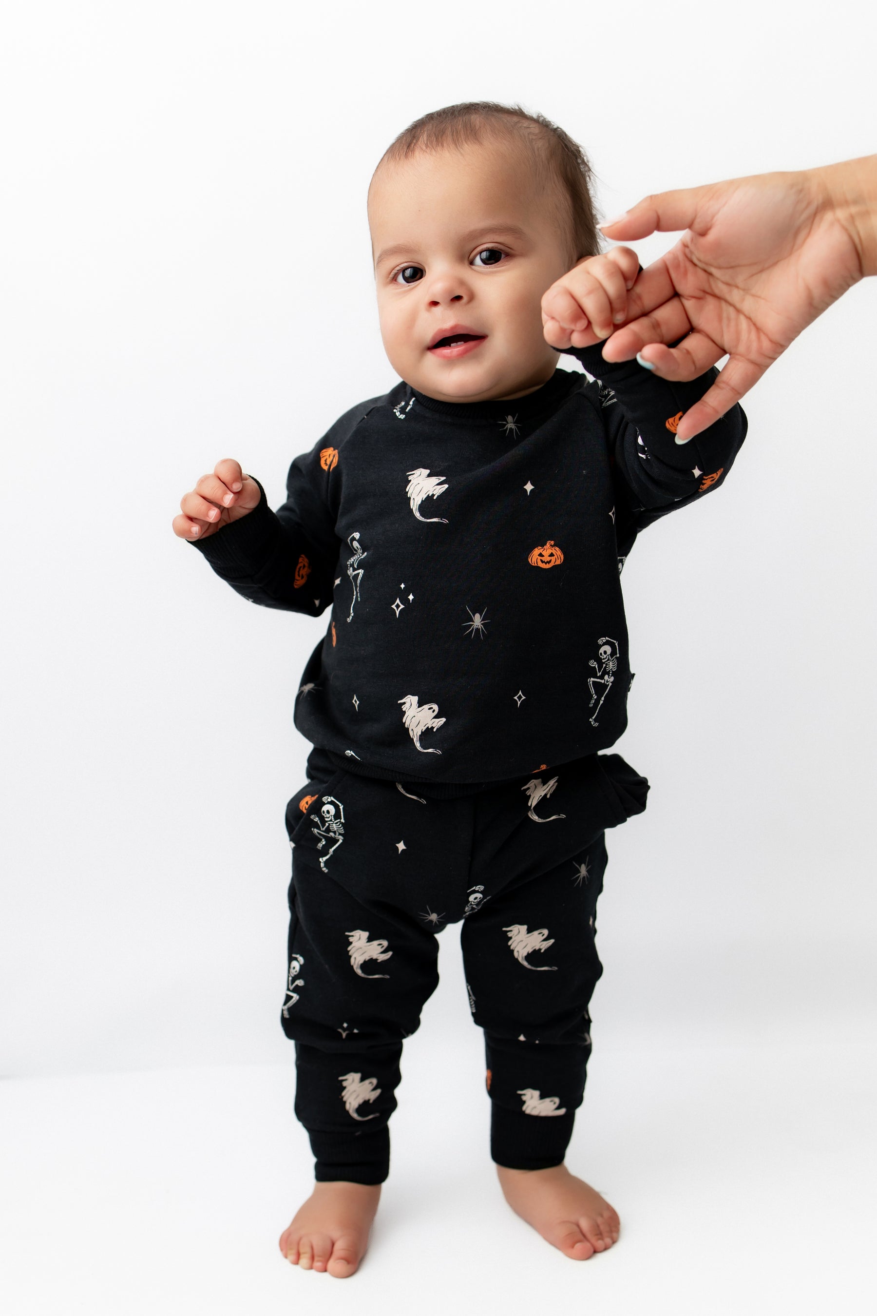Baby wearing Long Sleeve Jogger Set in Halloween Friends print standing holding an adult's hand on a white background