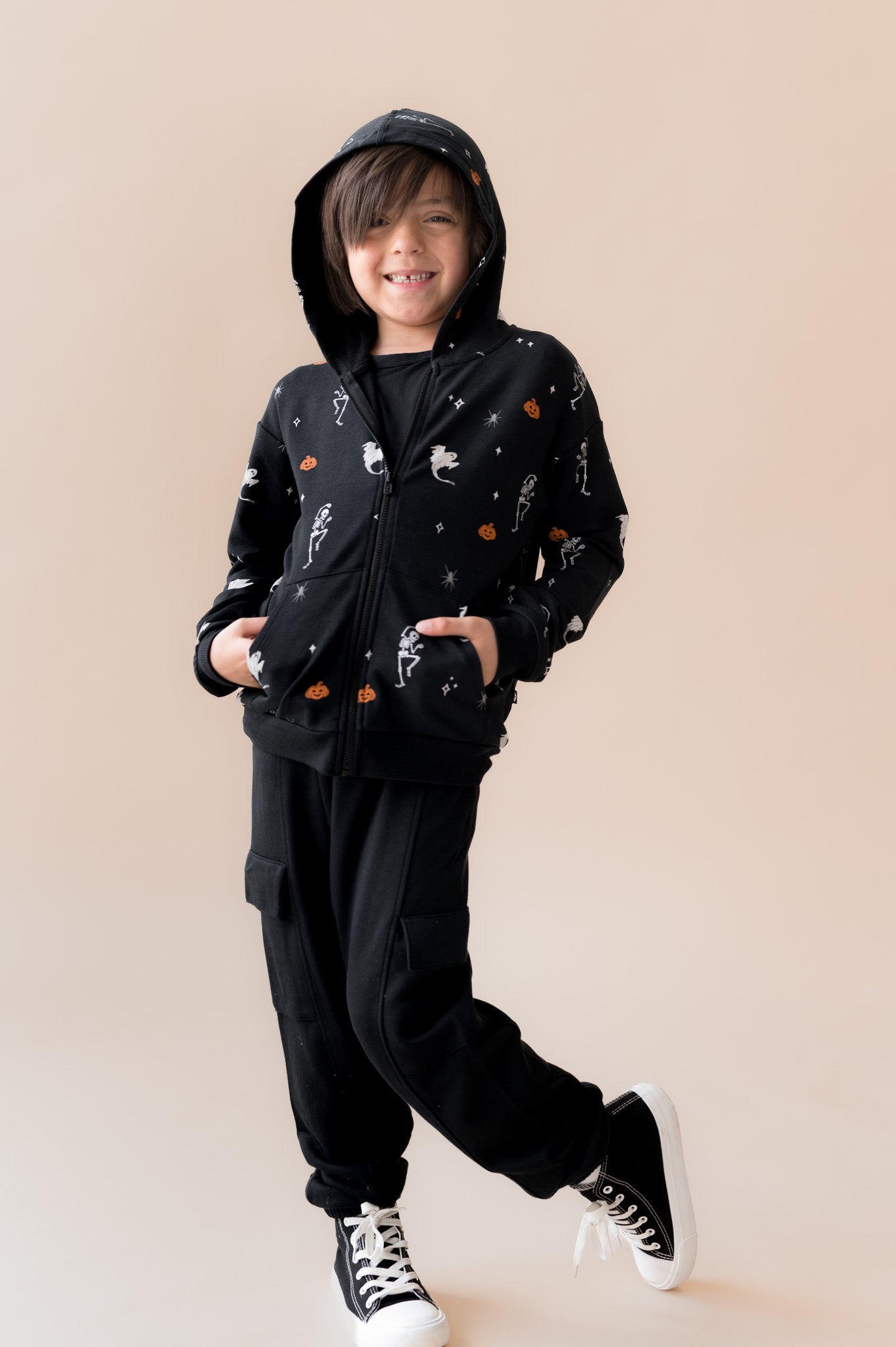 Boy posing in Zip-Up Hoodie in Halloween Friends print over black pants on a beige background