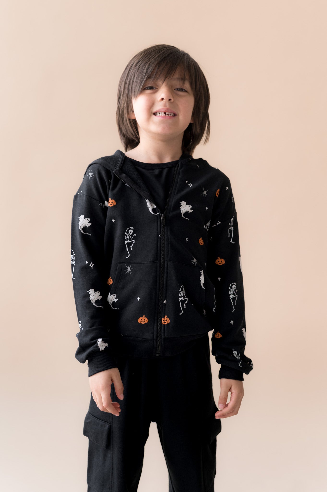 Boy smiling in Zip-Up Hoodie in Halloween Friends print over black pants on a beige background