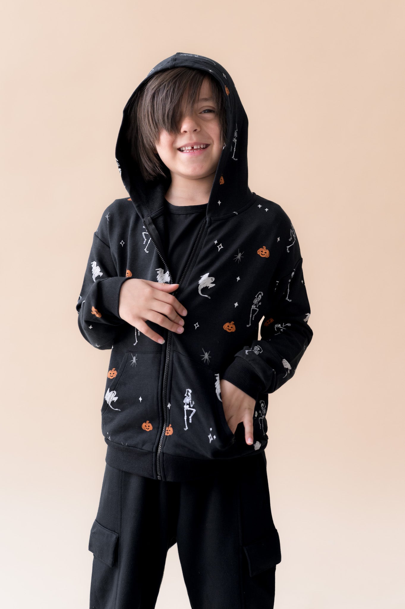 Boy wearing Zip-Up Hoodie in Halloween Friends print over black pants on a beige background