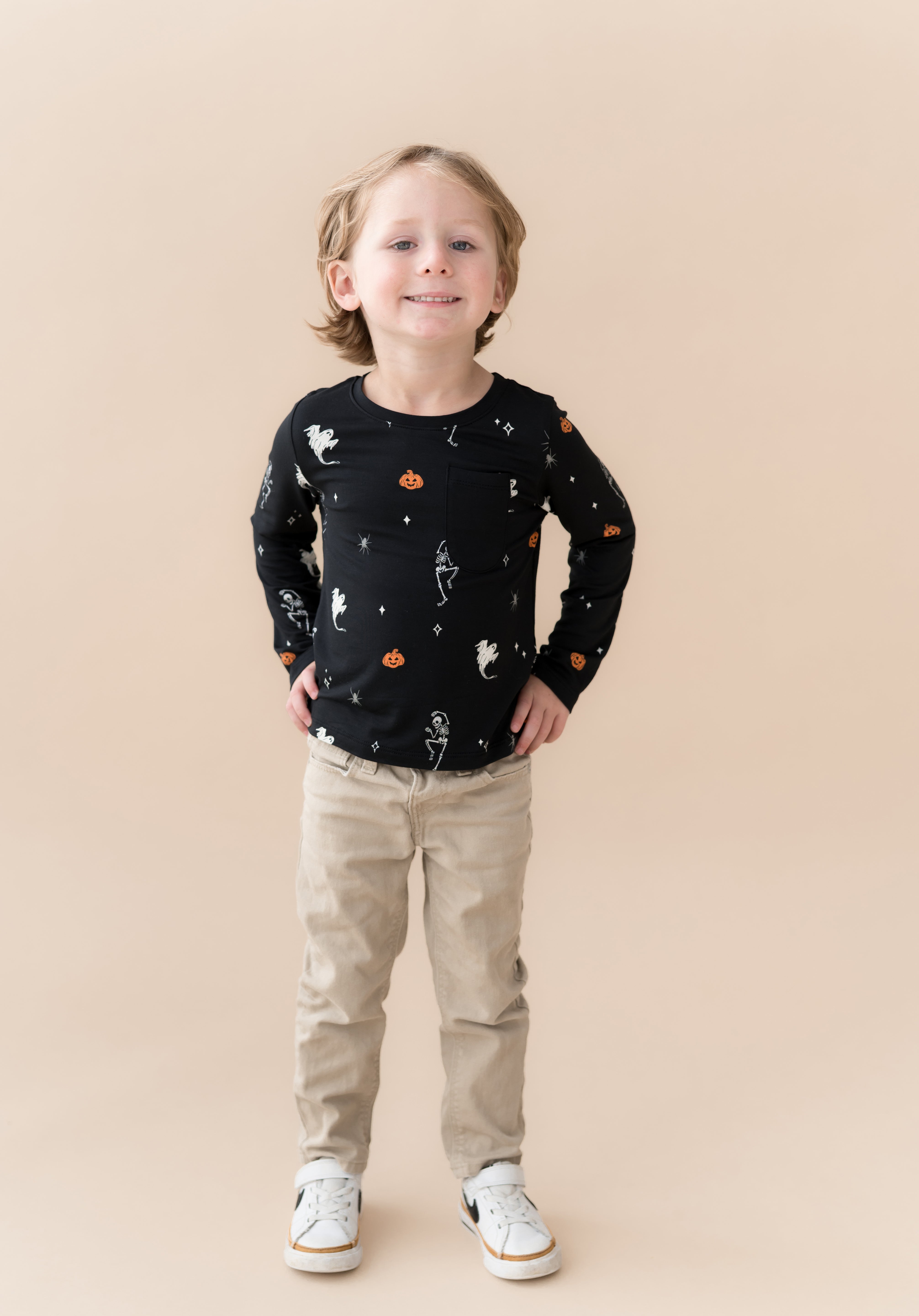 Boy smiling in Long Sleeve Toddler Crew Neck Tee in Halloween Friends print over beige pants on a beige background