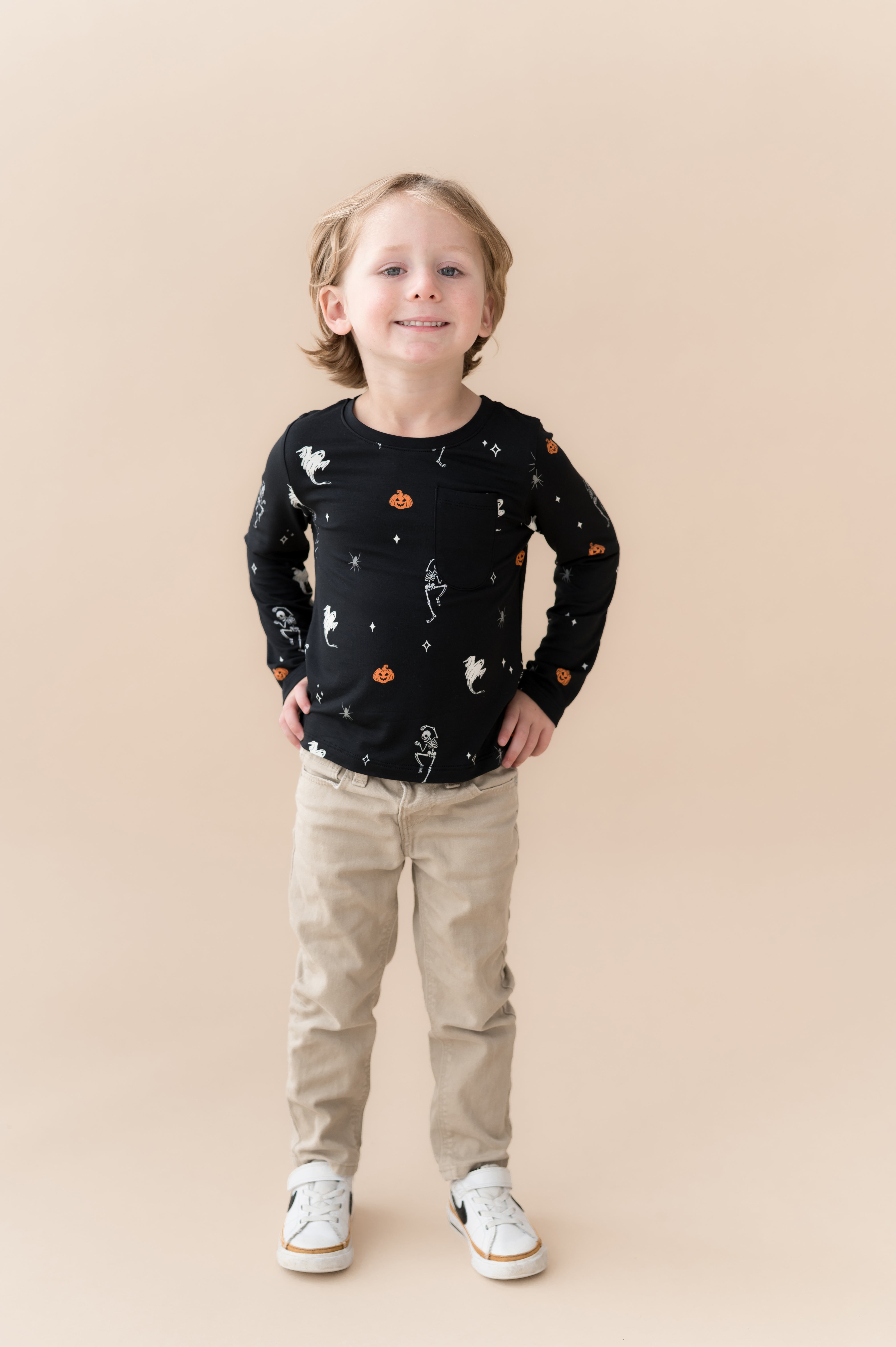 Boy smiling in Long Sleeve Toddler Crew Neck Tee in Halloween Friends print over beige pants on a beige background