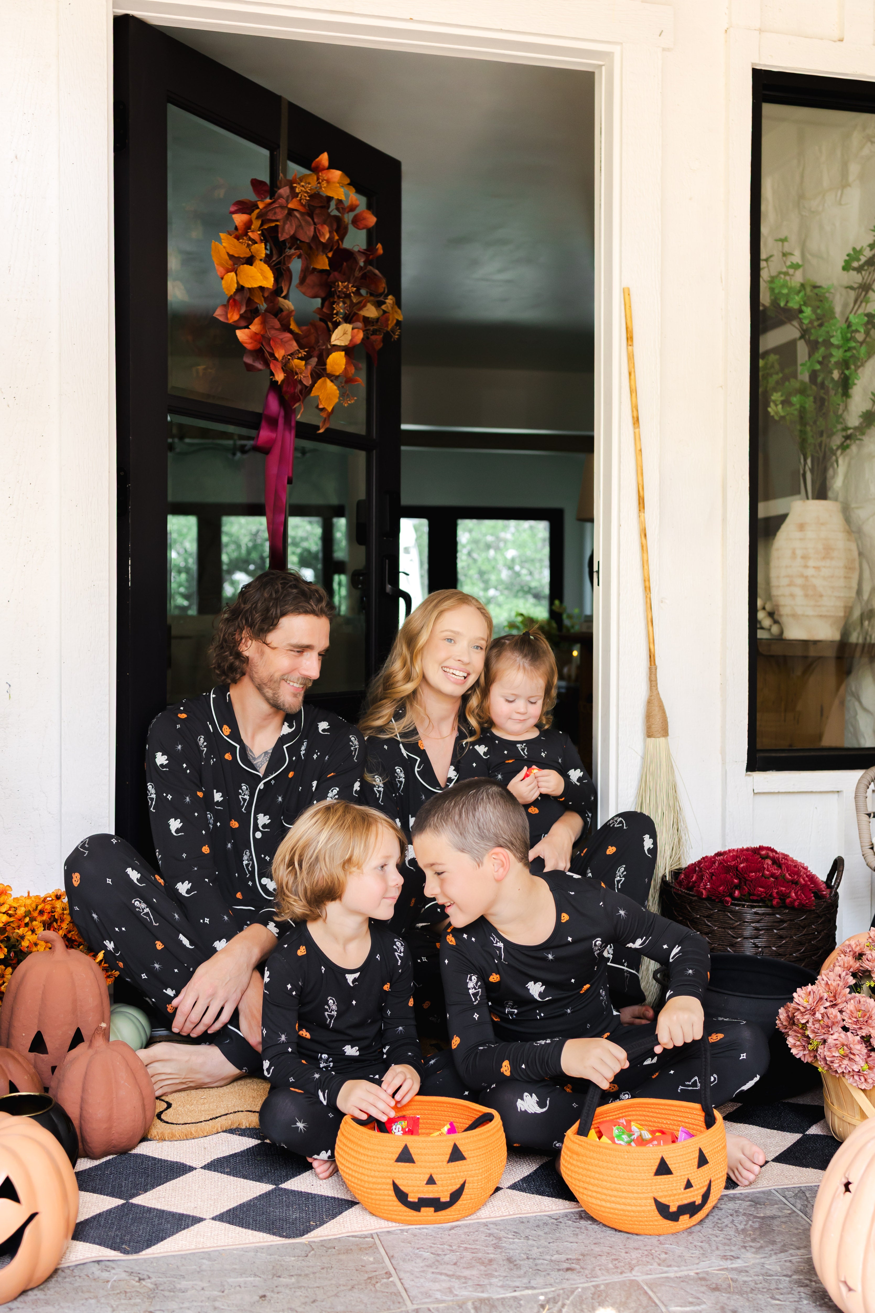 Family of five wearing Long Sleeve Pajama Sets in Halloween Friends print sitting in doorway with Halloween decorations