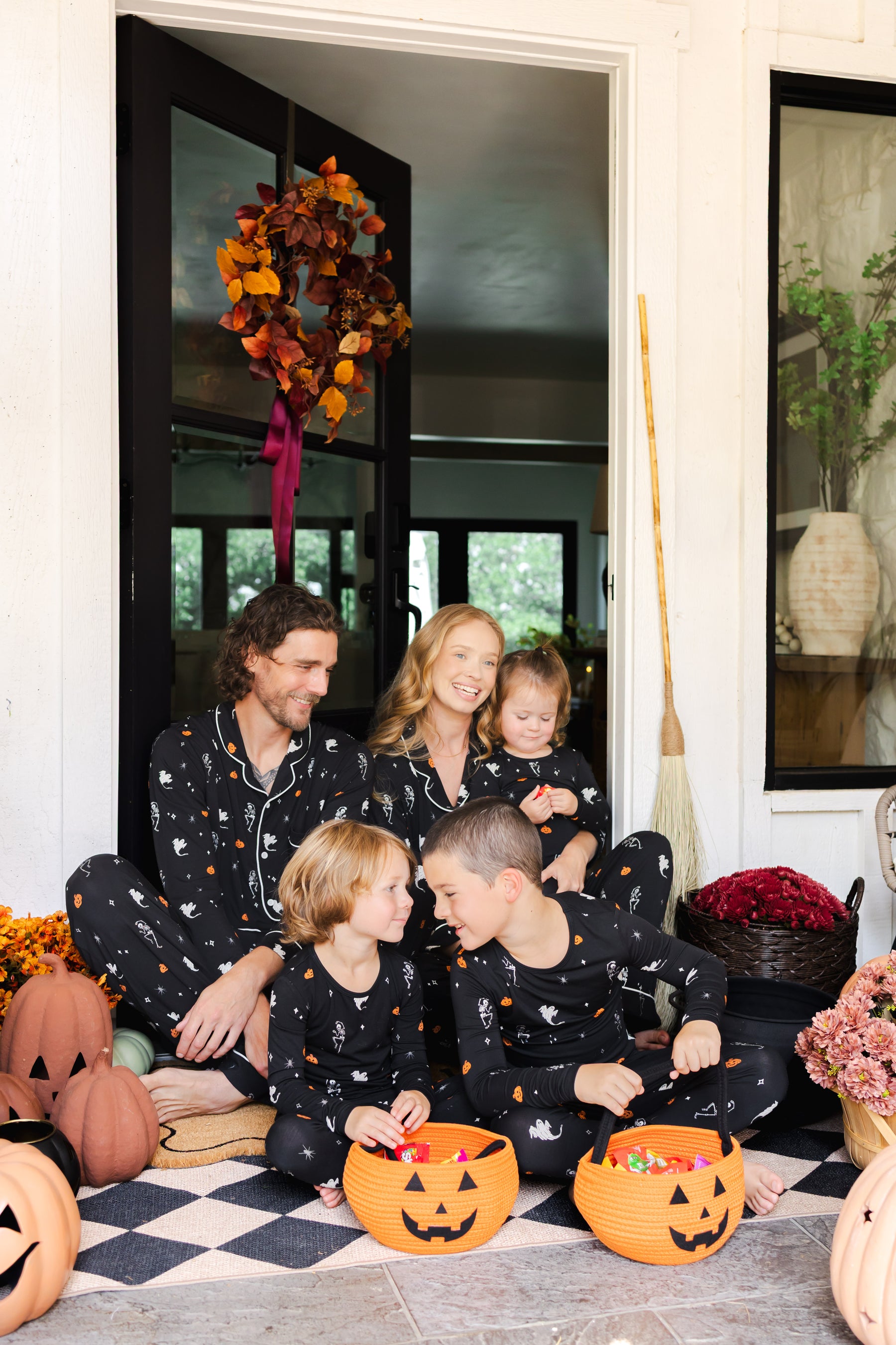 Family of five wearing Long Sleeve Pajama Sets in Halloween Friends print sitting in doorway with Halloween decorations