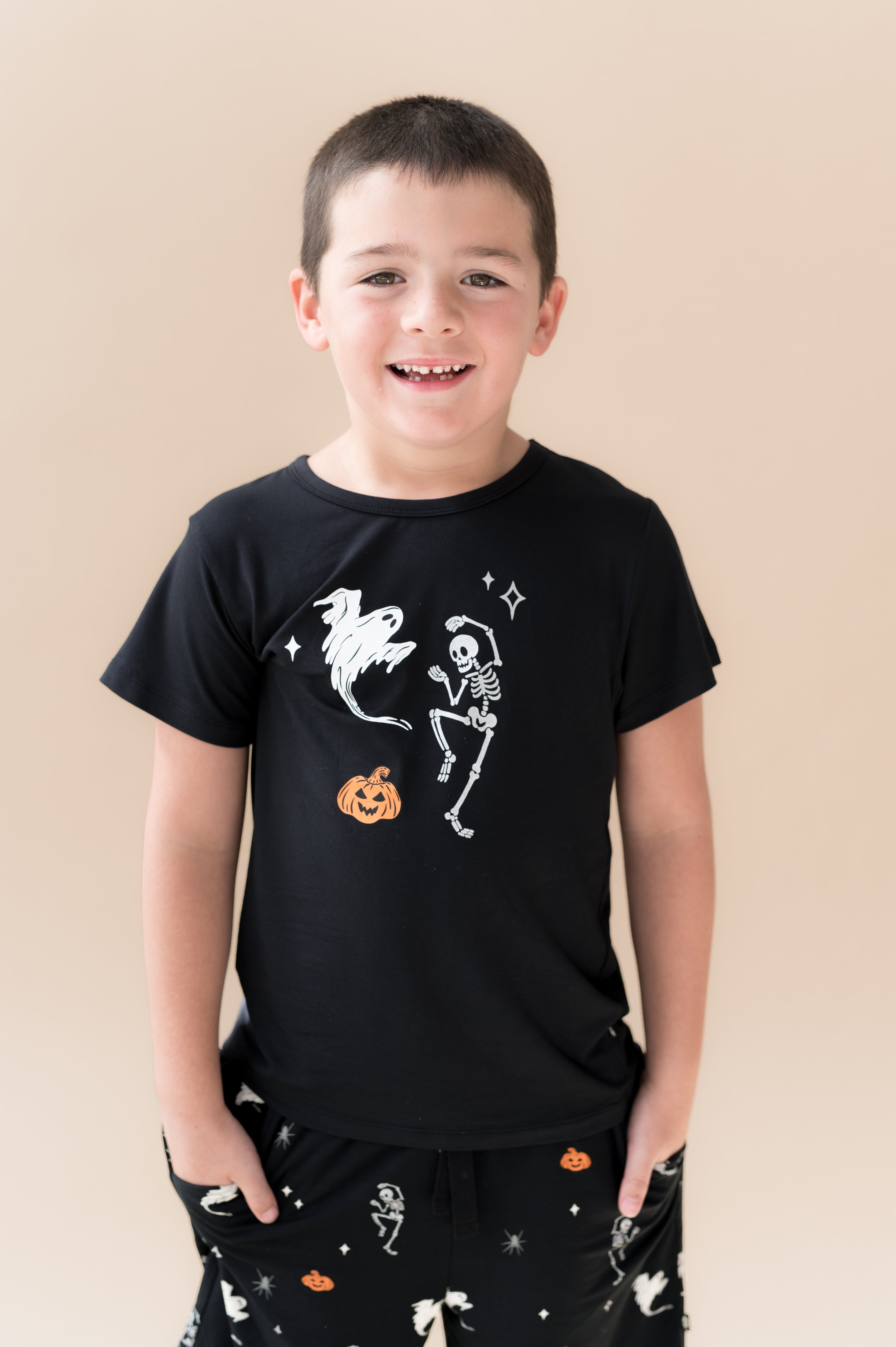 Boy wearing Black Toddler Basic Tee in Halloween Friends print in center over Similar print Drawstring shorts on a beige background