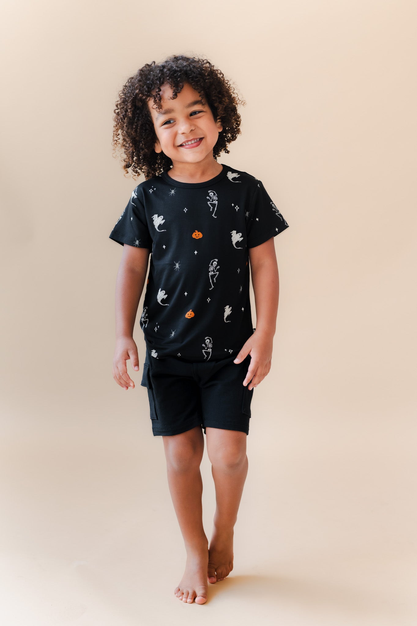 Boy posing in Toddler Basic Tee in Halloween Friends print over black shorts on a beige background