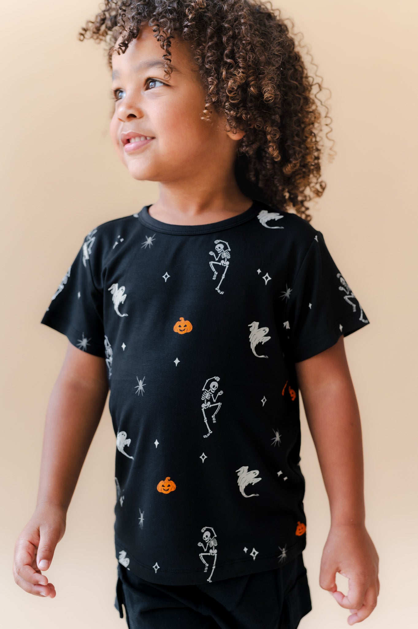 Boy wearing Toddler Basic Tee in Halloween Friends print over black shorts on a beige background