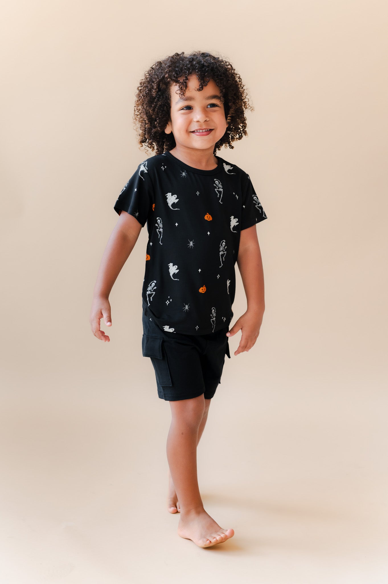 Boy posing in Toddler Basic Tee in Halloween Friends print over black shorts on a beige background