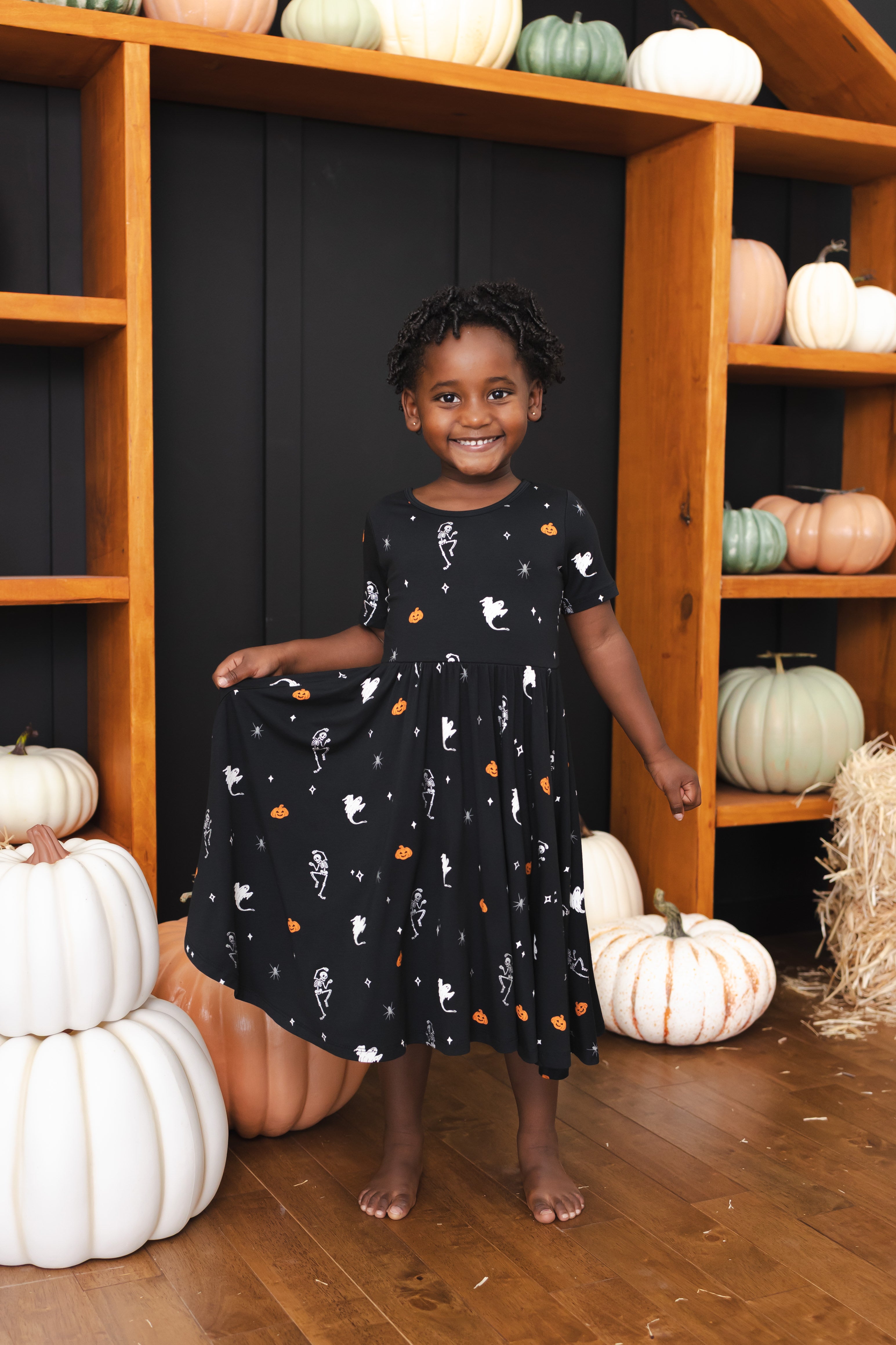 Girl wearing Twirl Dress in Halloween Friends print standing in front of Halloween decorations