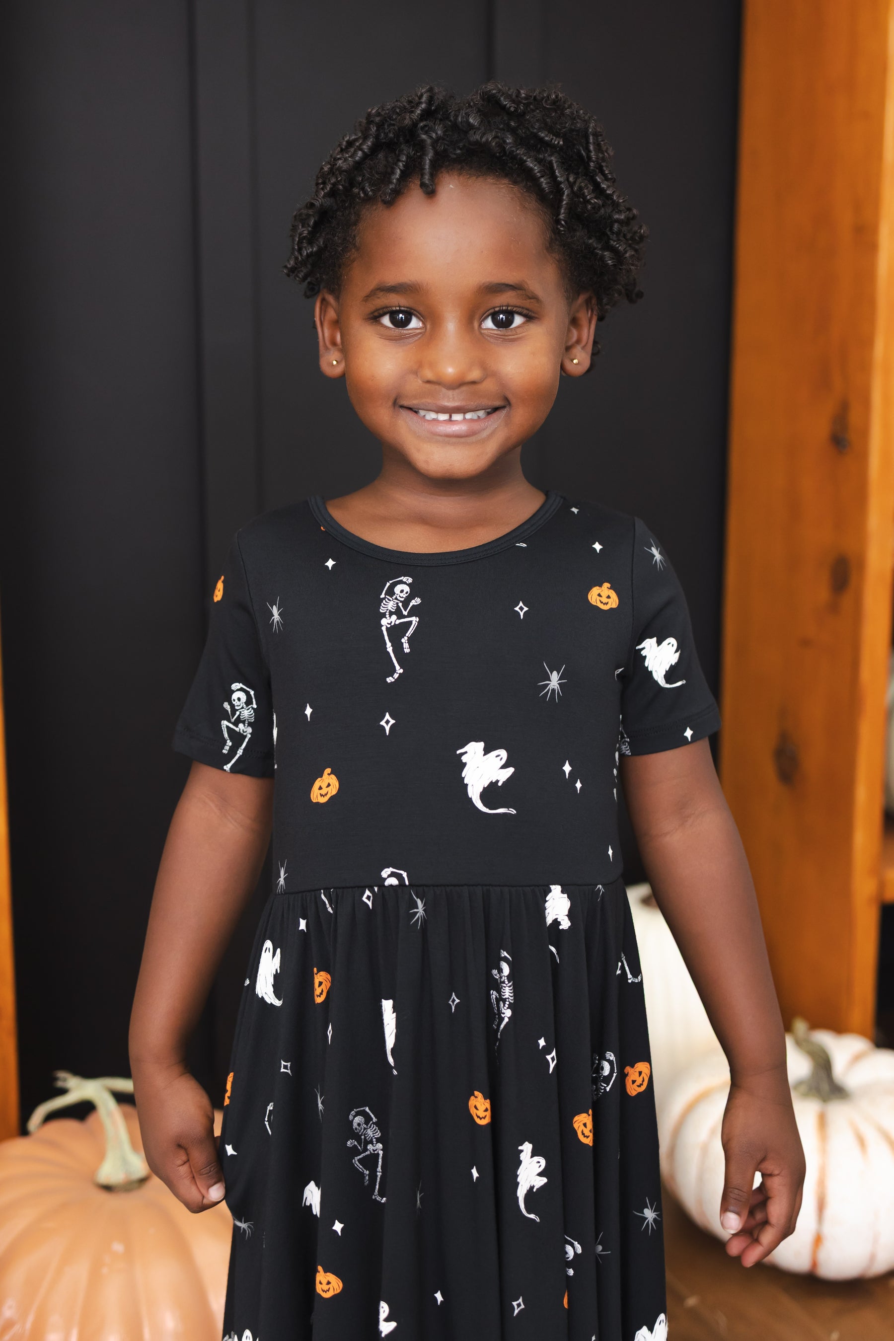 Girl smiling in Twirl Dress in Halloween Friends print standing in front of Halloween decorations