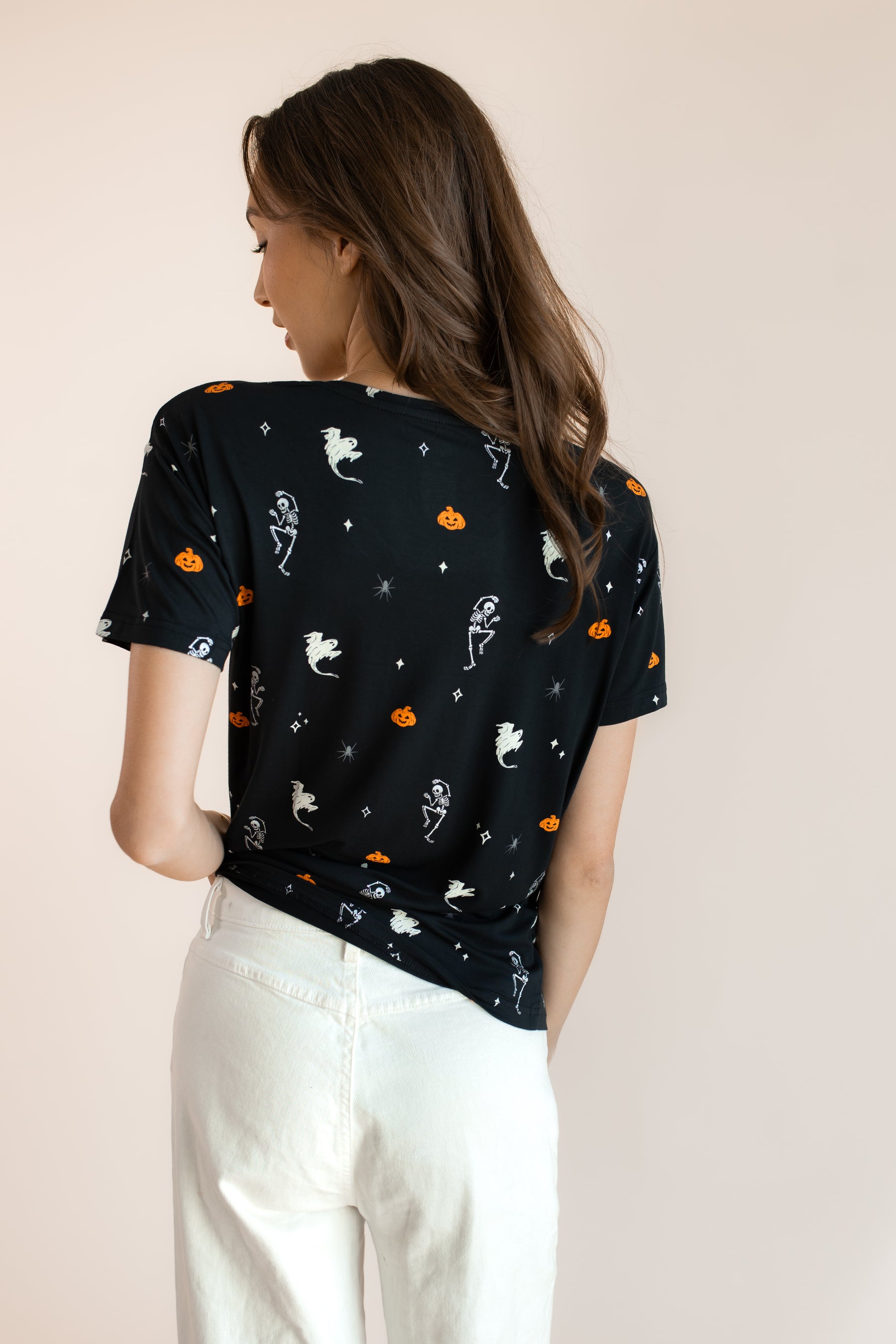 Back side of Modal wearing Women's Oversized V-Neck Tee in Halloween Friends print over white pants on a beige background