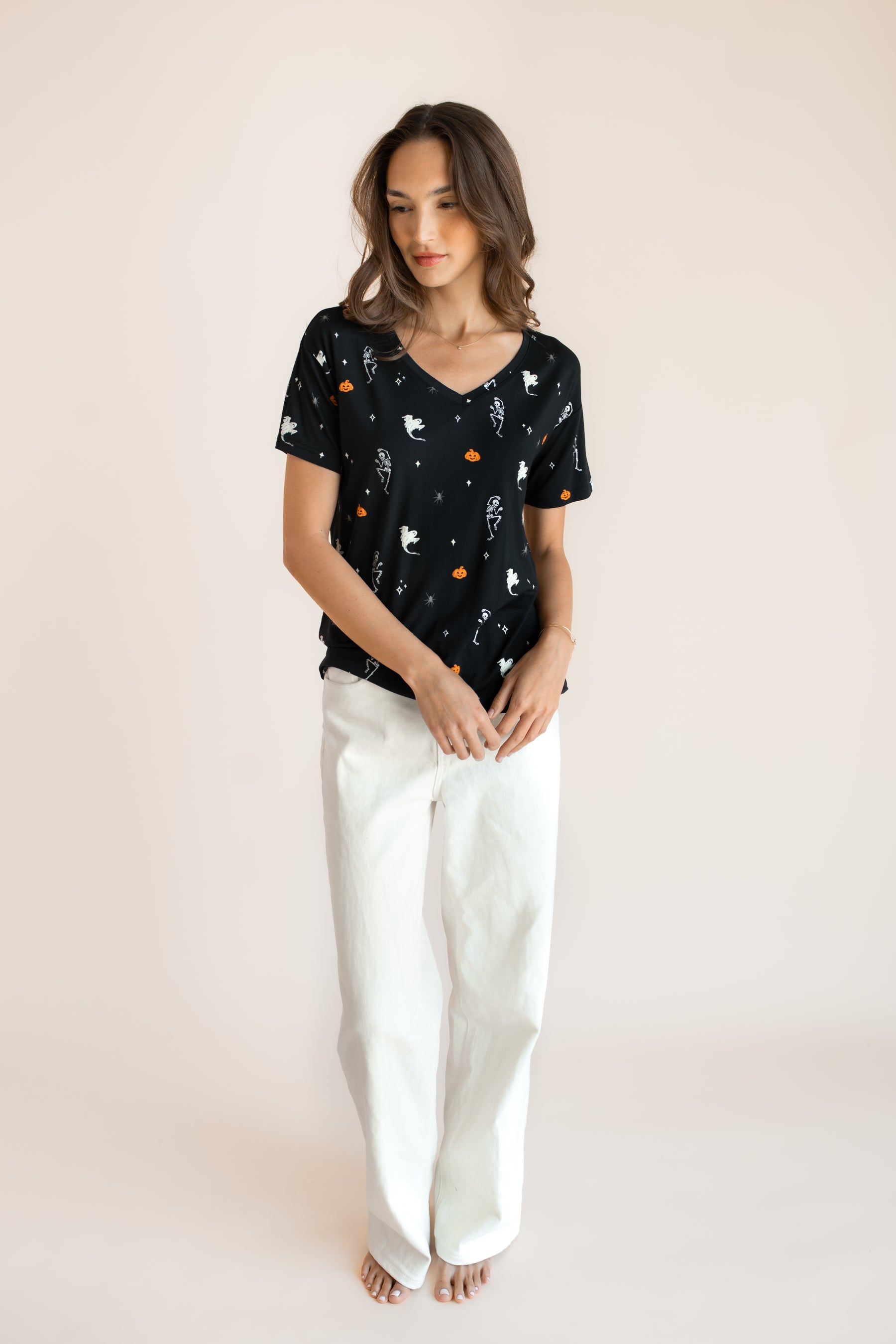 Modal posing in Women's Oversized V-Neck Tee in Halloween Friends print over white pants on a beige background