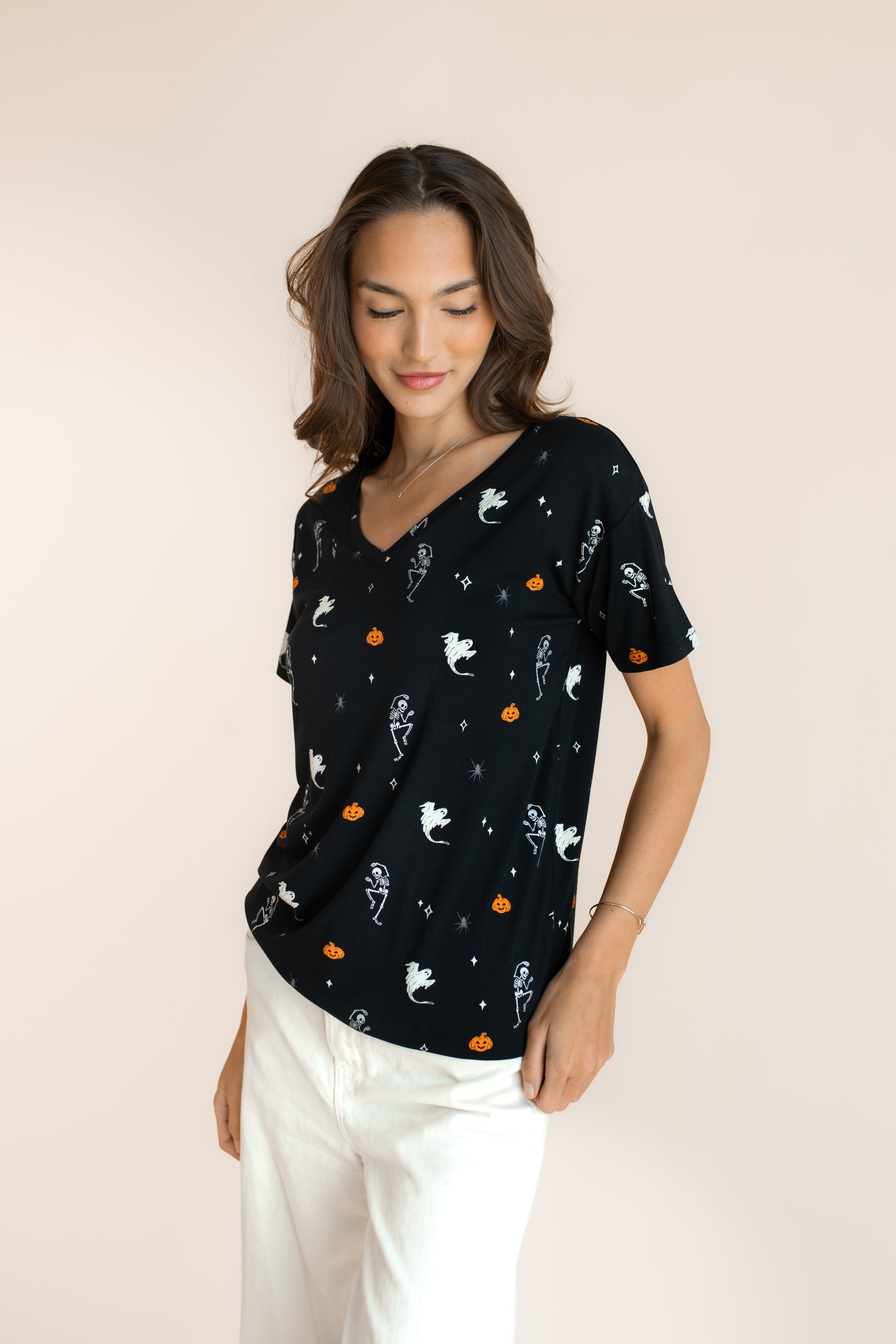 Close up of Modal in Women's Oversized V-Neck Tee in Halloween Friends print over white pants on a beige background