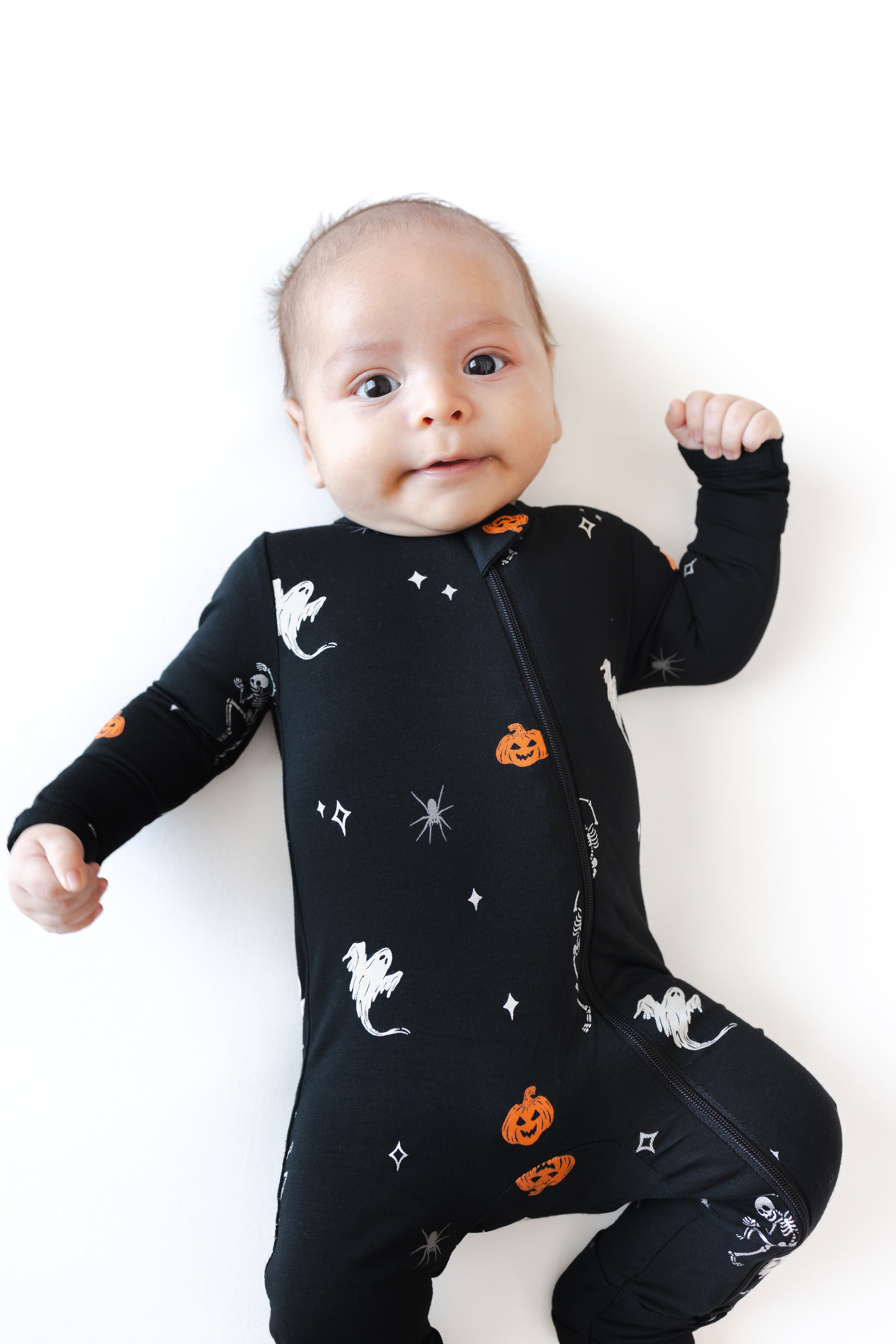 Close up of Baby wearing Zippered Romper in Halloween Friends print lying on a white background