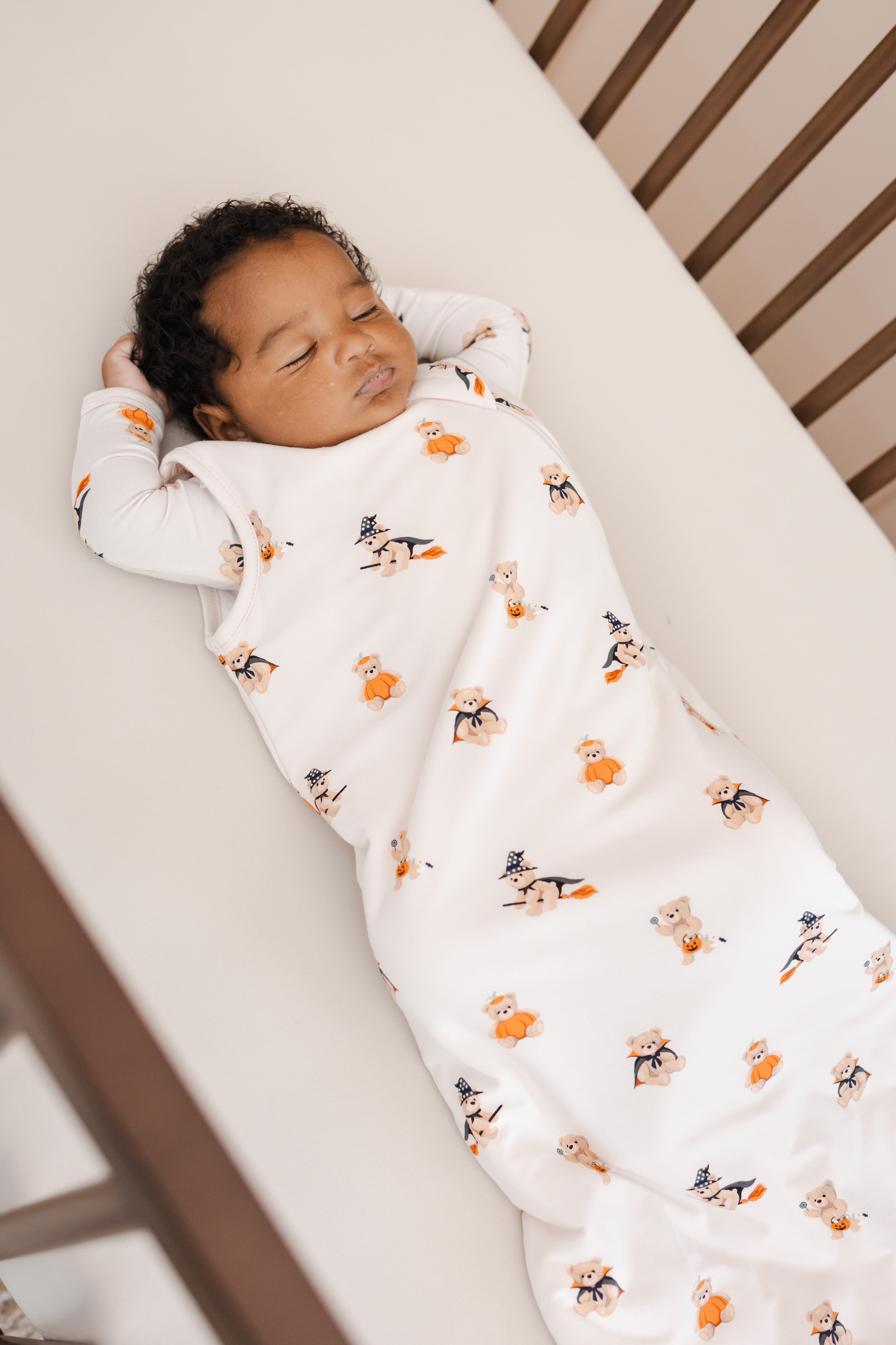 Baby sleeping in a crib wrapped in a Sleep Bag in Halloween Teddy 1.0 print on a beige crib sheet