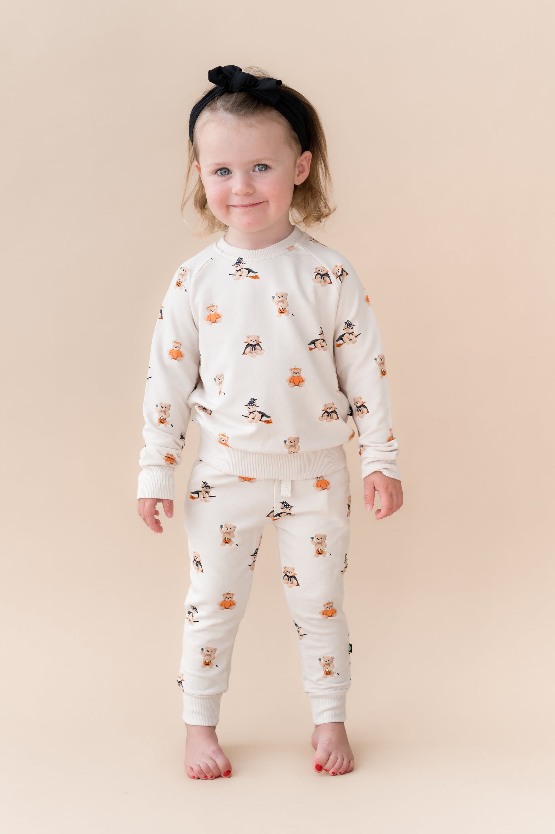 Girl wearing Beige Long Sleeve Jogger Set in Halloween Teddy print with a black bow on a beige background