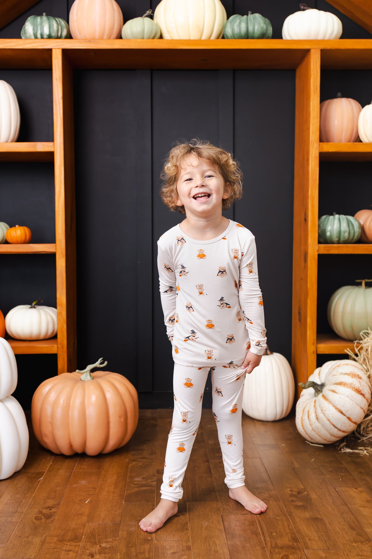 Boy wearing Long Sleeve Pajamas in Halloween Teddy print standing with Halloween pumpkin decorations