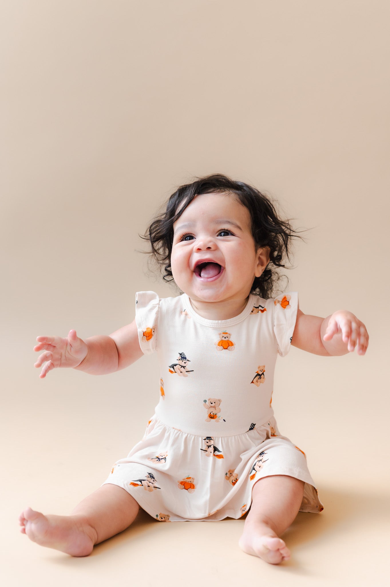 Baby wearing Twirl Bodysuit Dress in Halloween Teddy print on a beige background