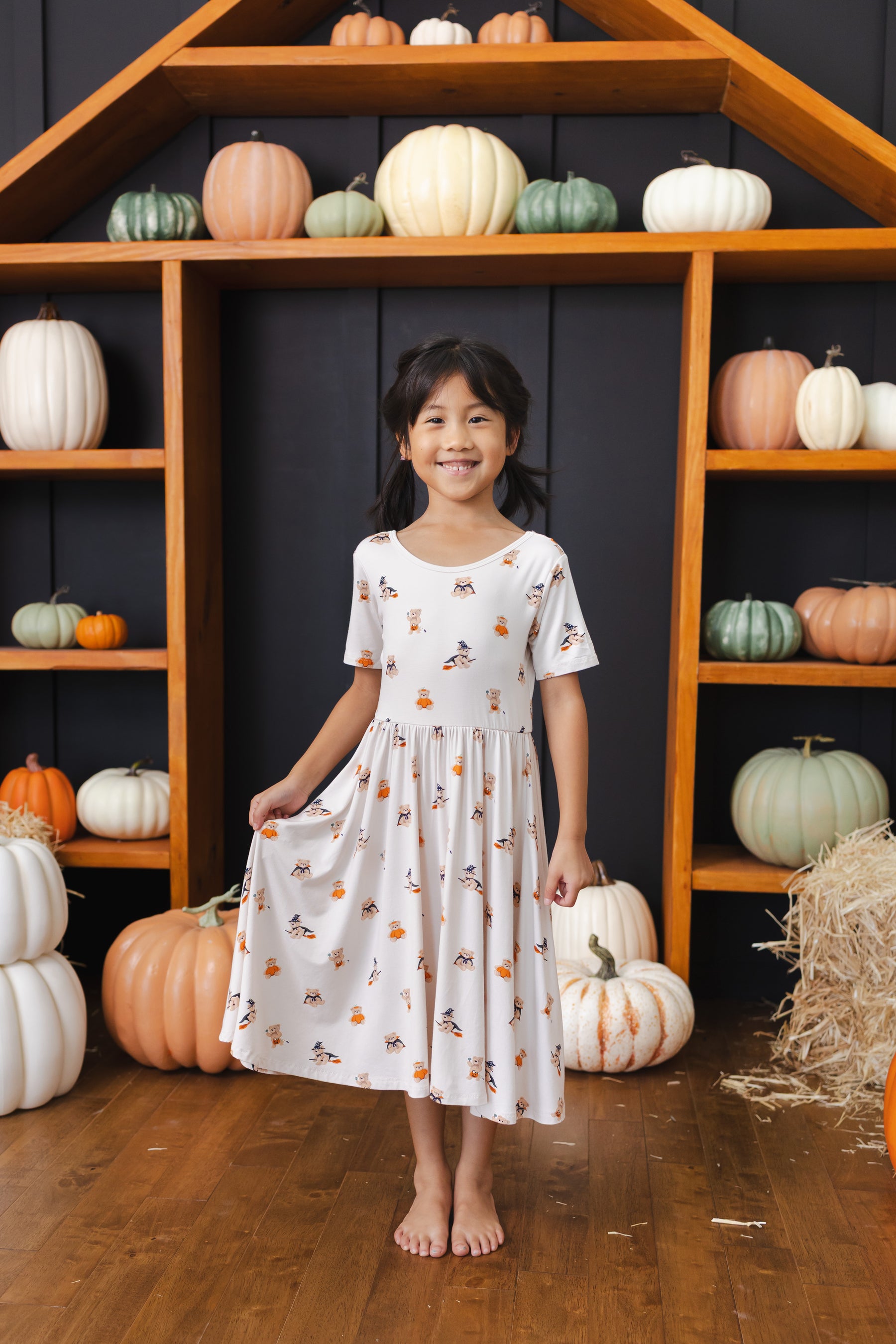 Girl wearing Twirl Dress in Halloween Teddy print standing in front of pumpkin Halloween decorations around