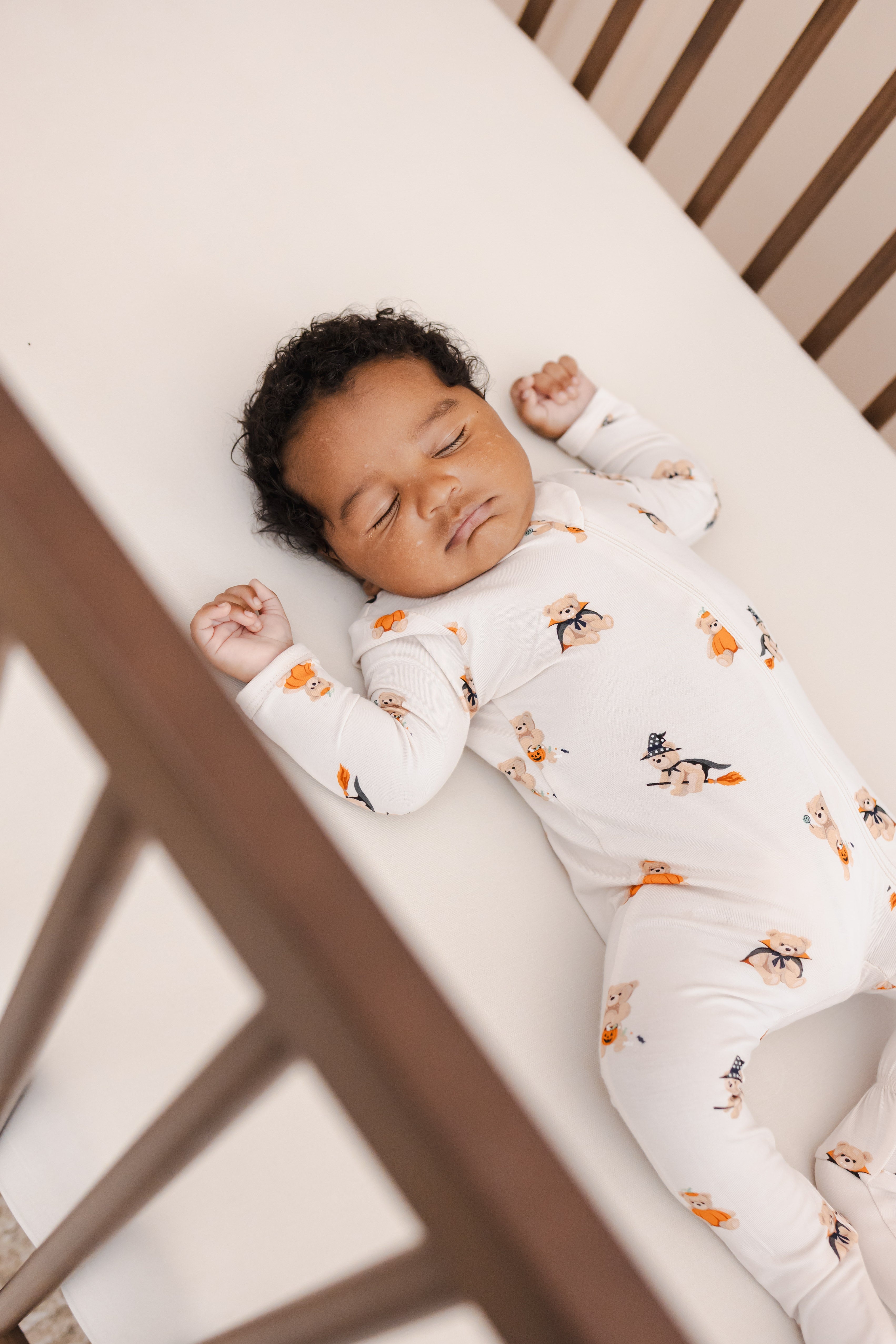 Baby sleeping in crib wearing Zippered Footie in Halloween Teddy print on a beige crib sheet