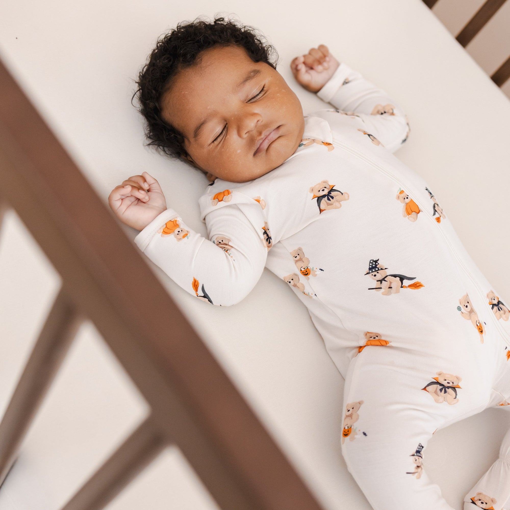Baby in a halloween teddy bear printed footie pajama laying in a crib